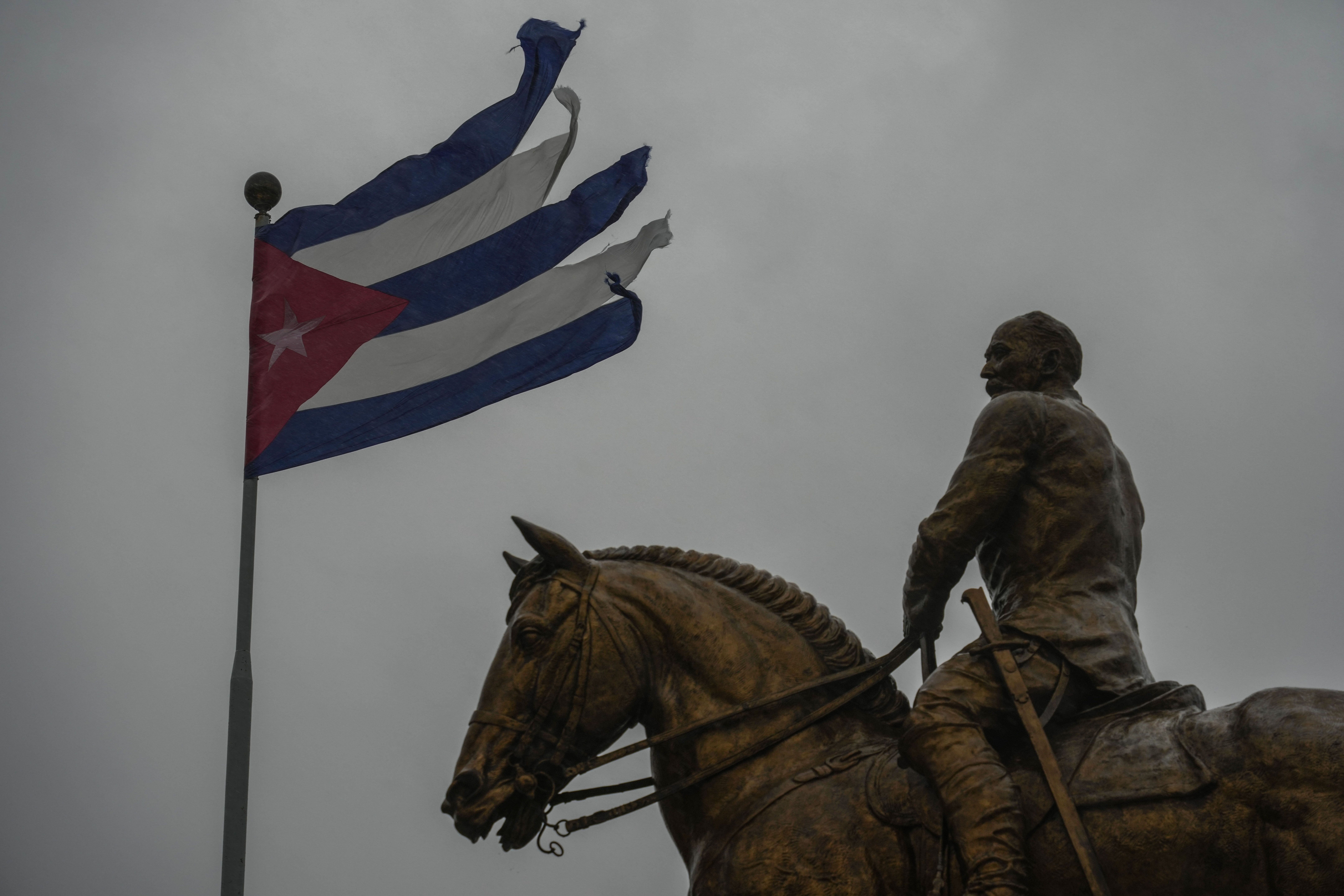 A man on horseback rides under a tattered Cuban flag.