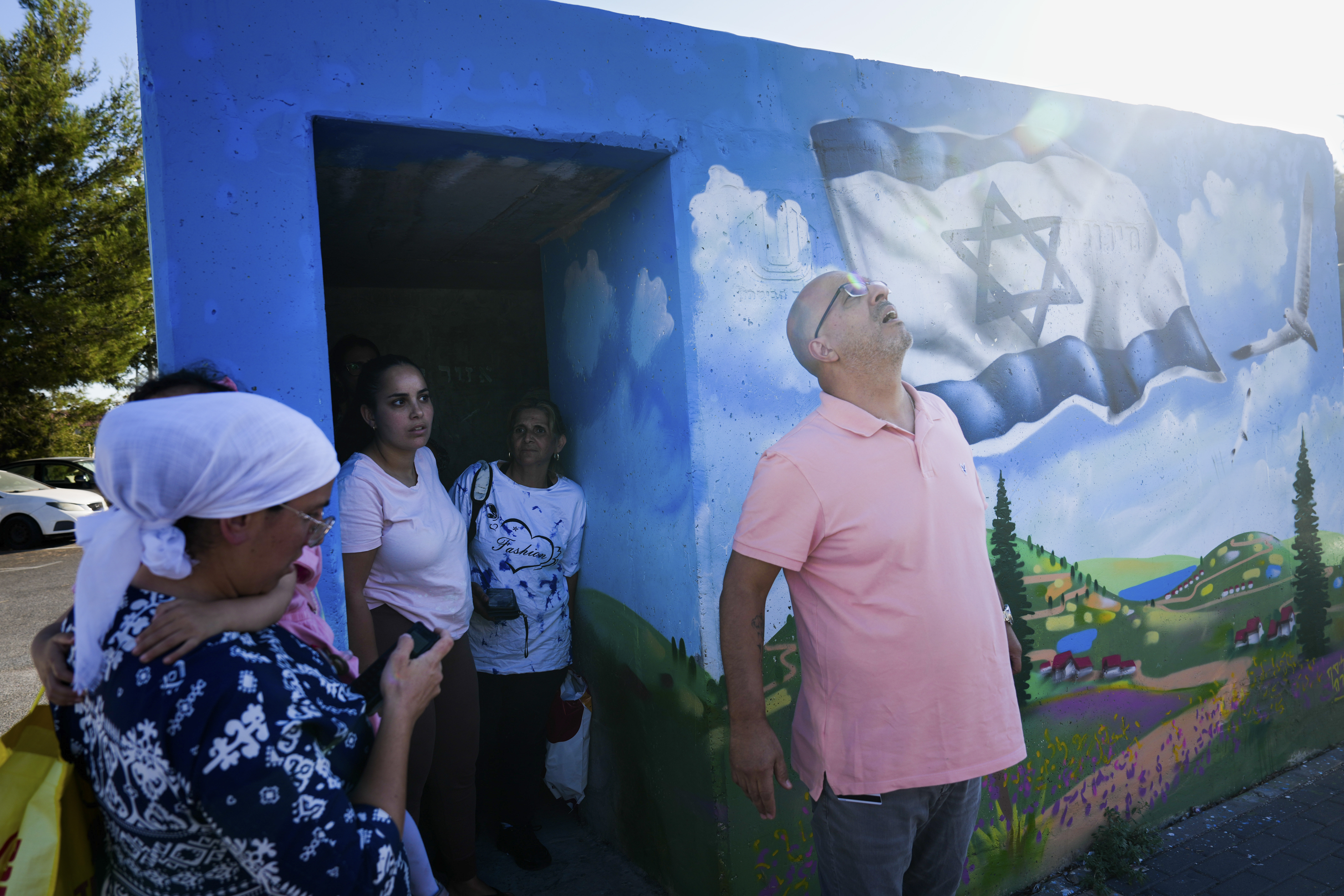 People take cover next to a public bomb shelter as a siren sounds a warning of incoming rockets fired from Lebanon