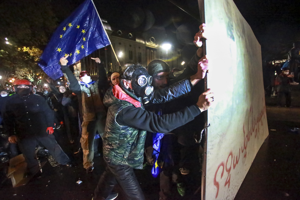 People with an EU flag hold a part of a fence as police use a water cannon against protesters.