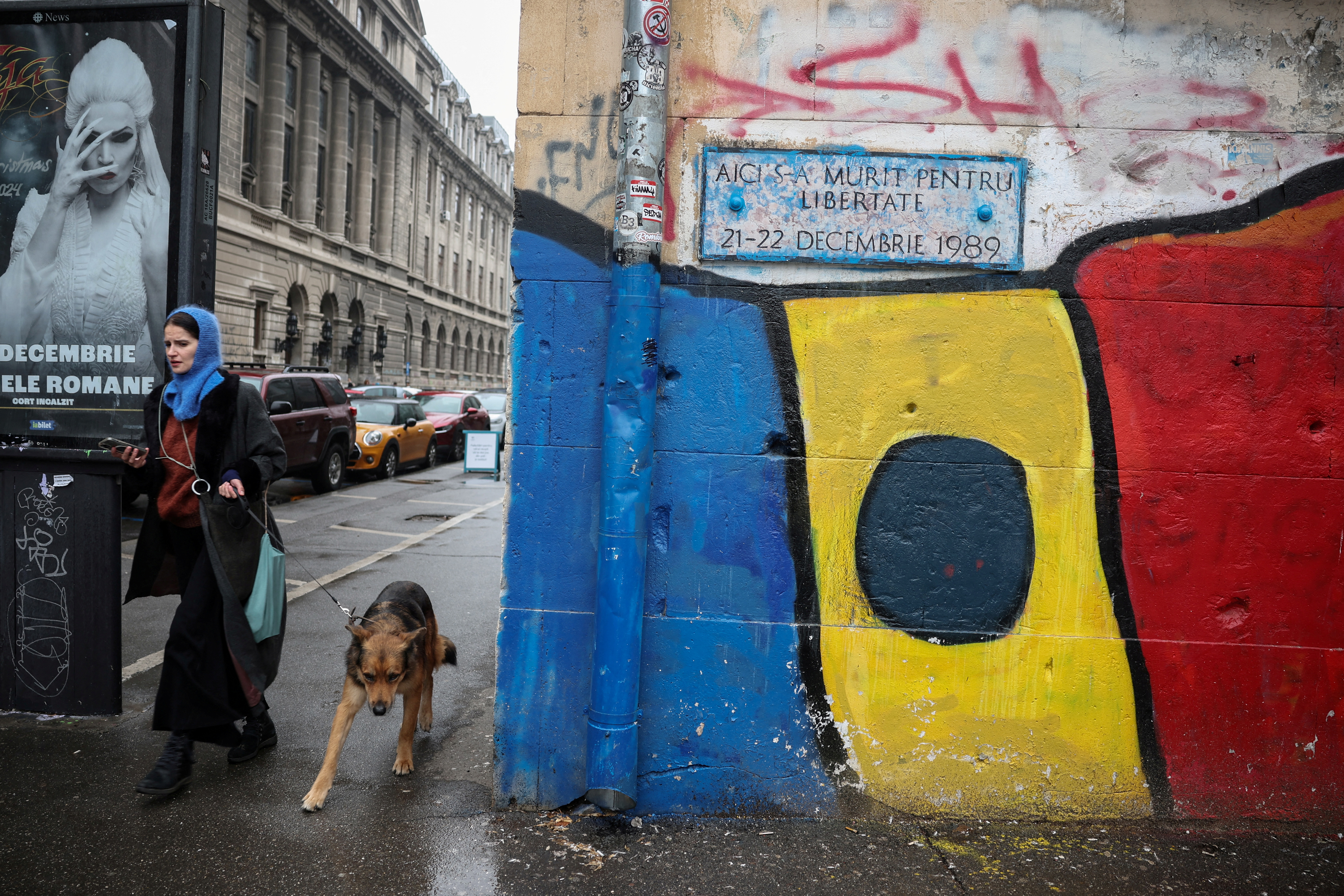 A woman walks her dog past a mural depicting the Romanian flag