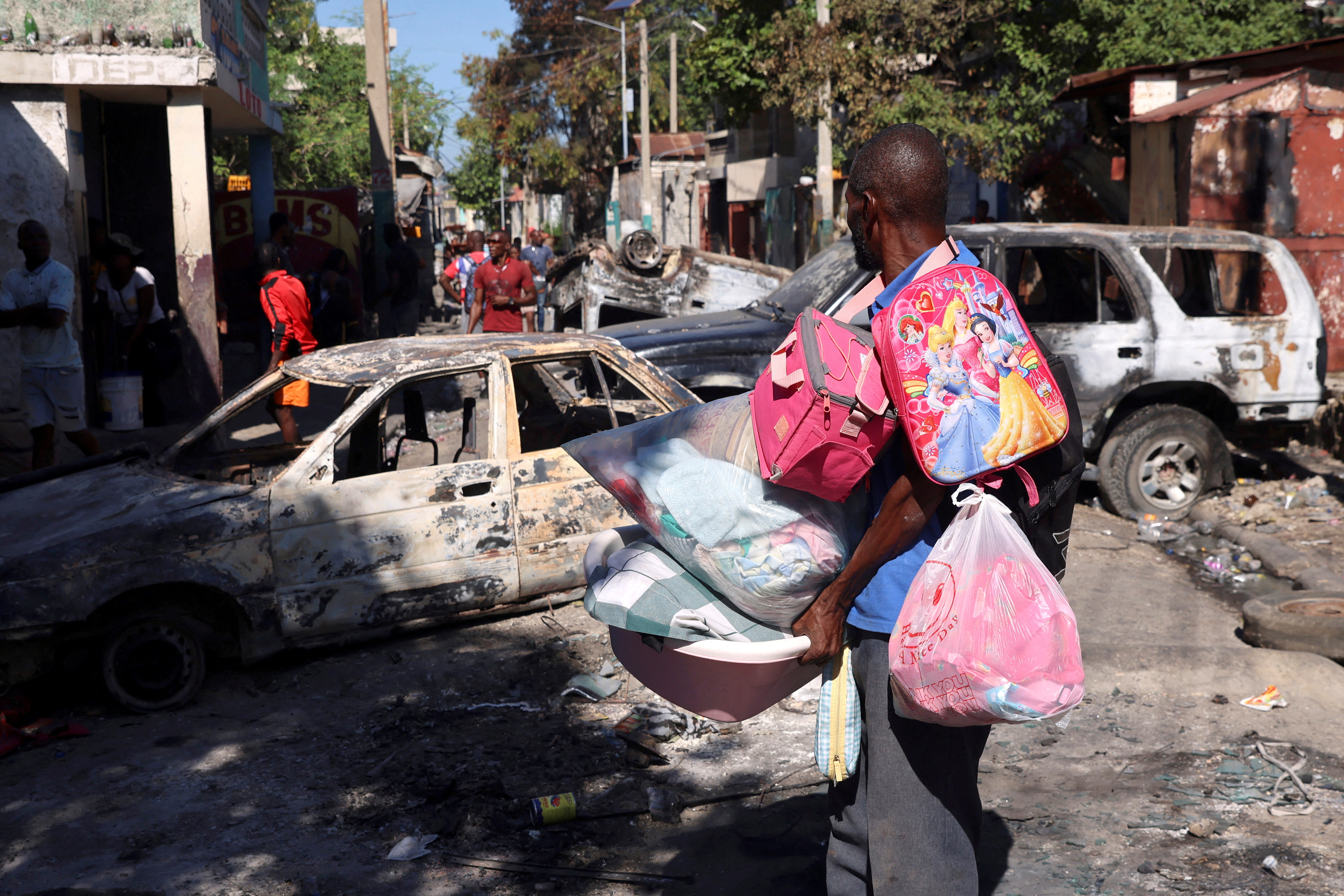 A man carrying his belongings observes the wreckages of vehicles burnt over the weekend by armed gangs, many grouped behind an alliance known as Viv Ansanm, as he flees the Poste Marchand suburb, in Port-au-Prince, Haiti