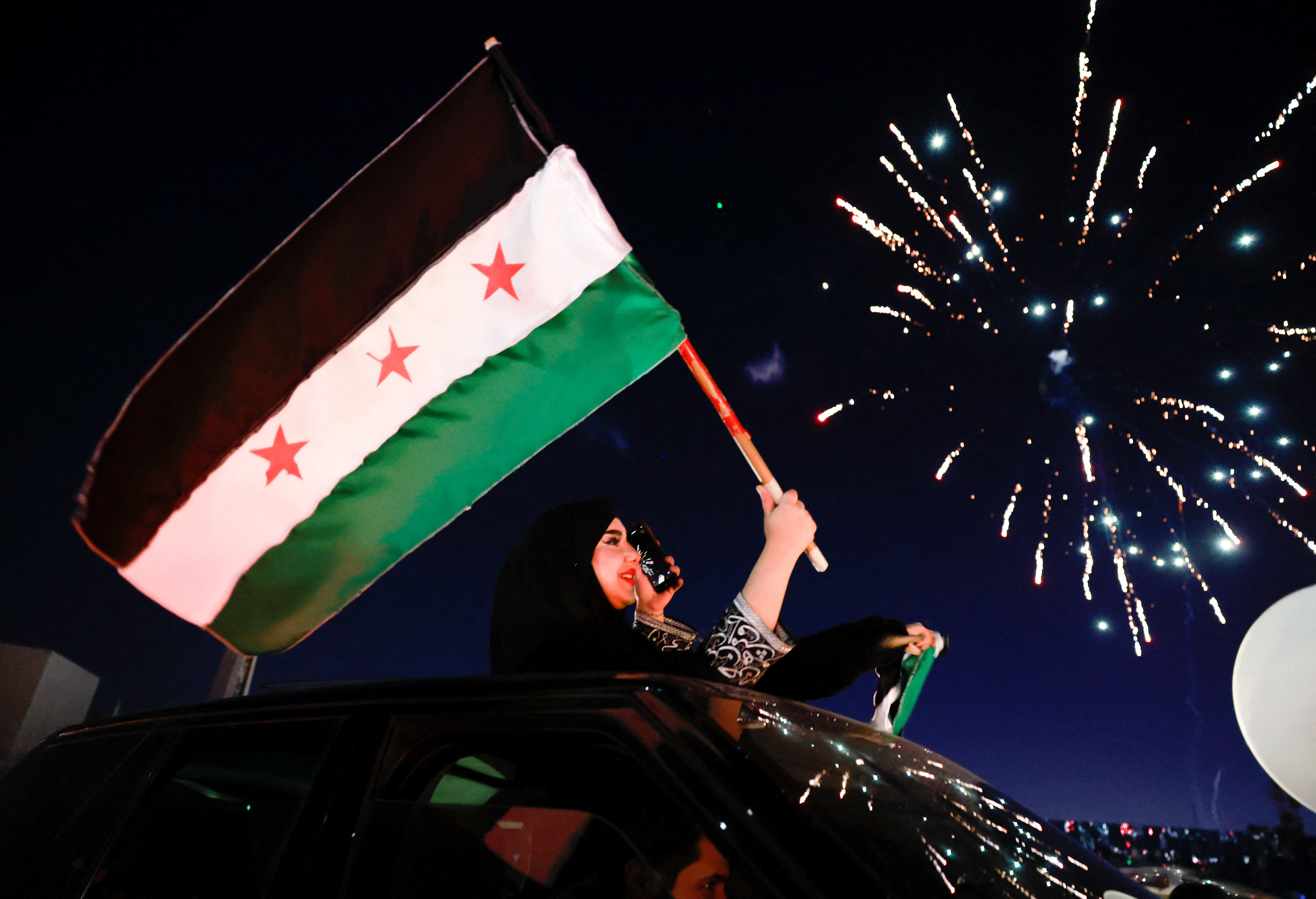 A woman holds up a flag adopted by the new leaders of Syria.