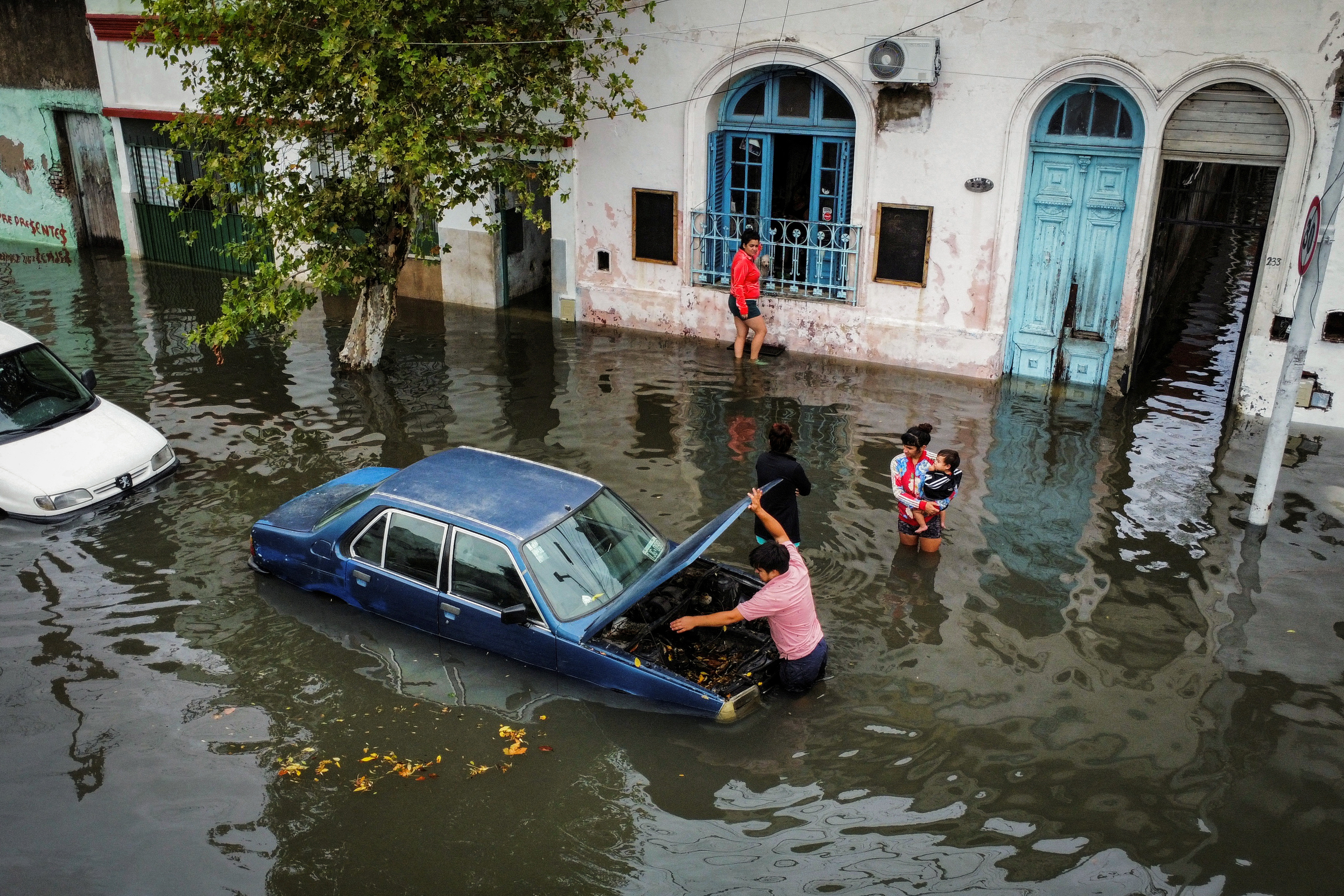 A drone view shows a man working on a car, partially submerged by floods caused by heavy rains, as people stand nearby, in Avellaneda, in the outskirts of Buenos Aires, Argentina, March 12