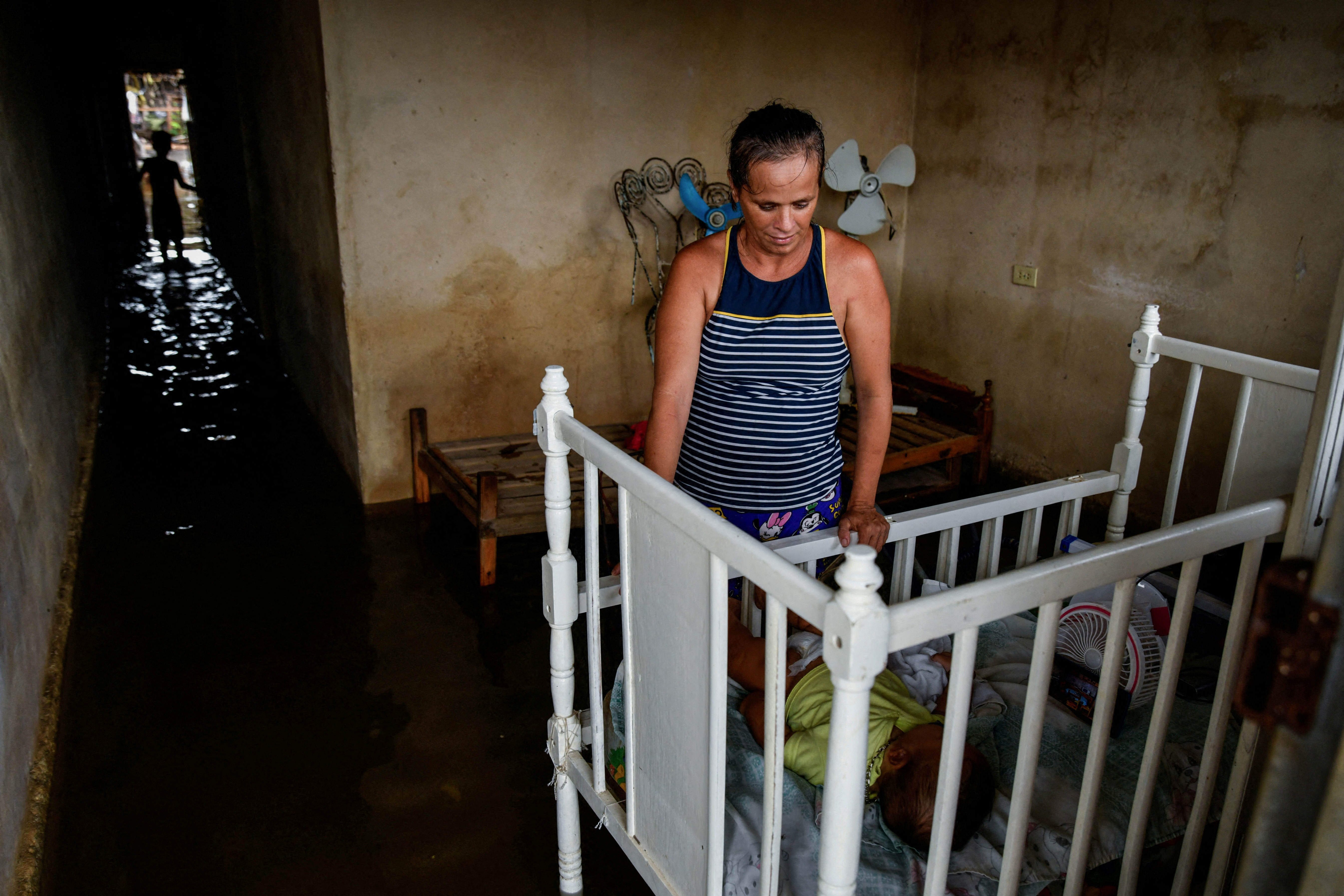 A woman checks on a baby inside a flooded house as Hurricane Milton passes close to the Cuban coast, in Batabano, Cuba, October 9, 2024