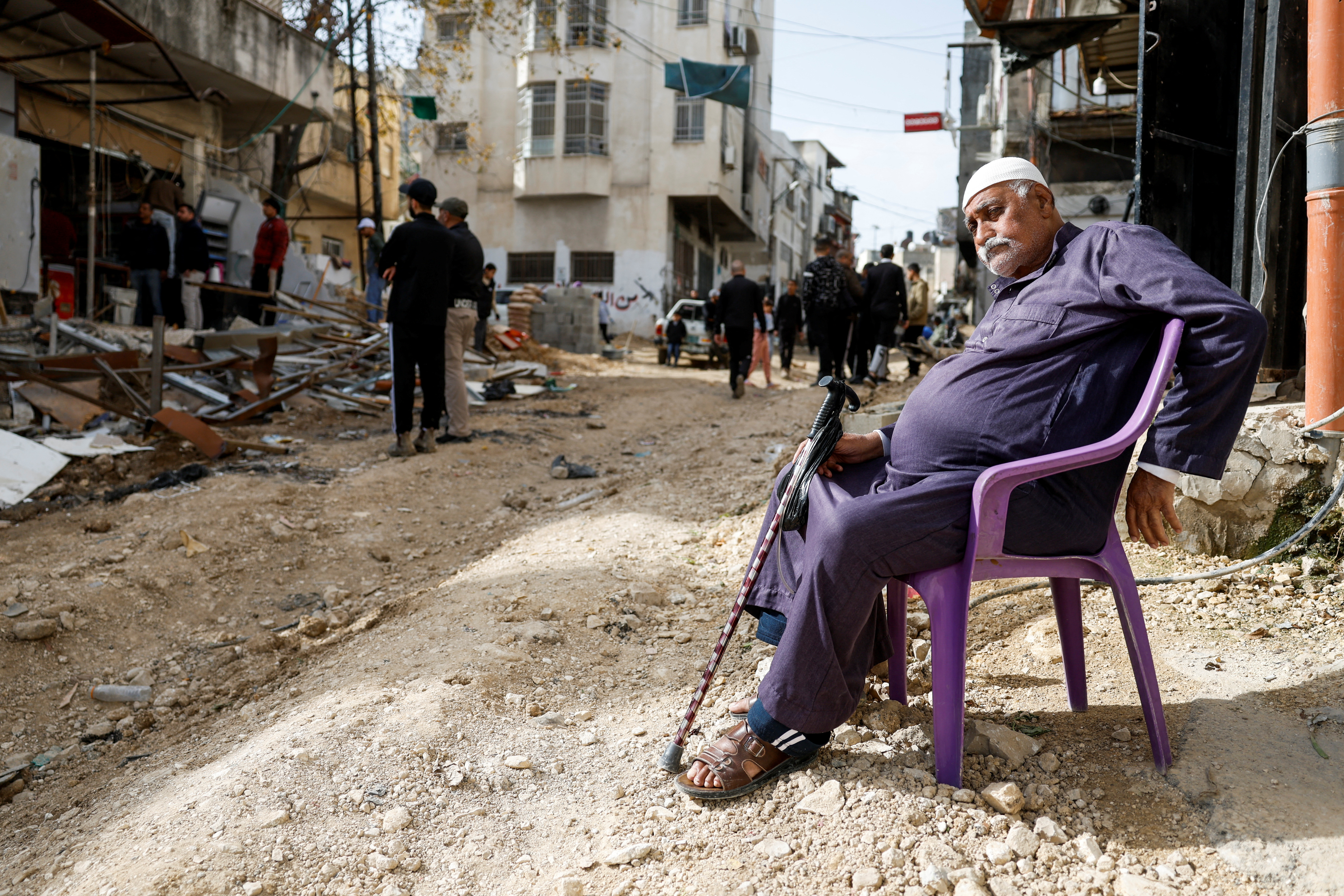 A Palestinian man sits on a chair in a damaged road, following an Israeli military raid, in Tulkarm, in the Israeli-occupied West Bank [File: Mohammed Torokman/Reuters]