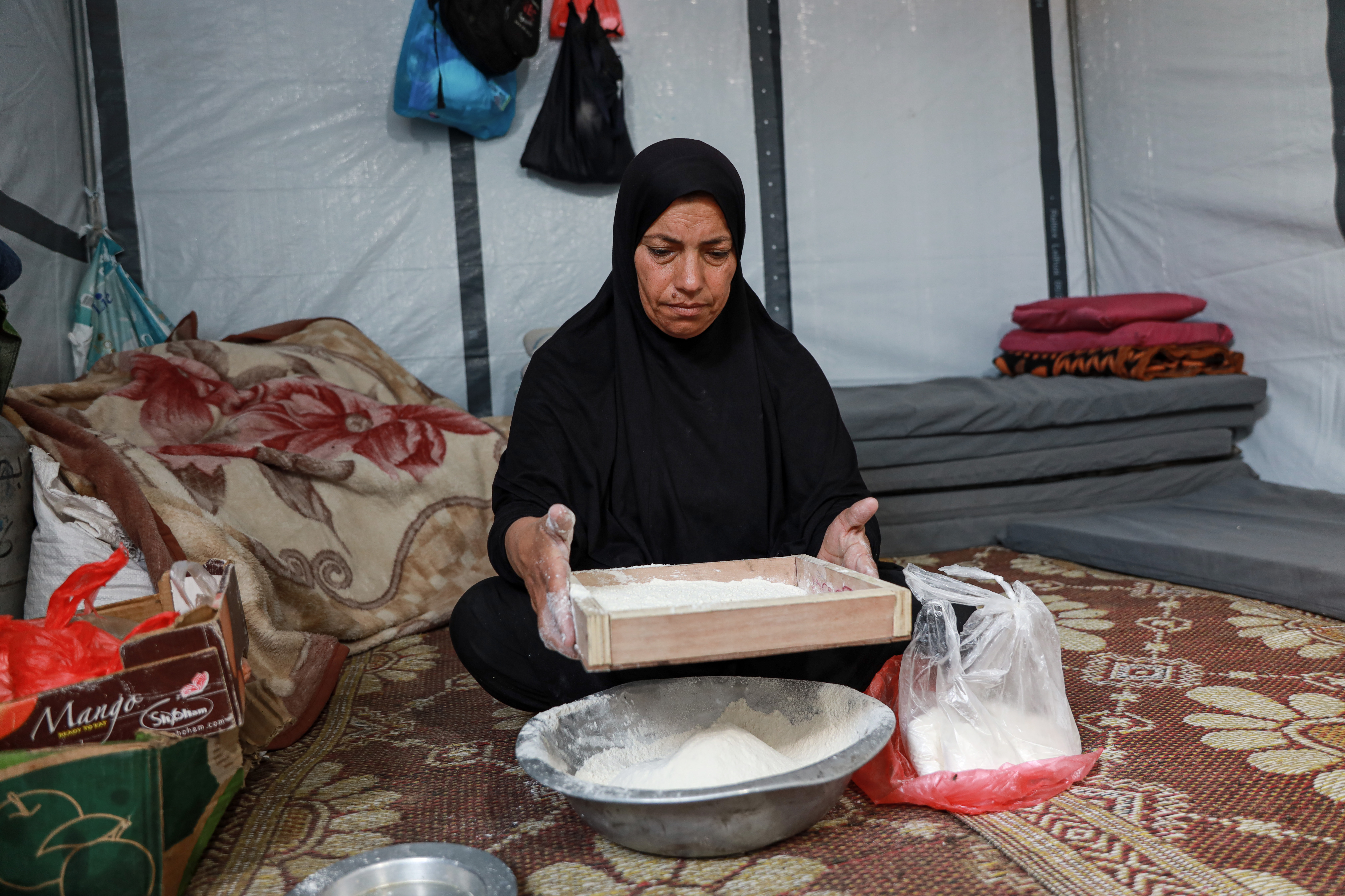 Fadia Wadi sifts the flour full of weevils before kneading it [Abdelhakim Abu Riash/Al Jazeera]