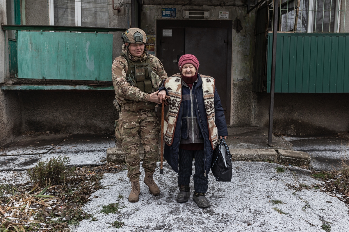a soldier helps an elderly woman walk through snow