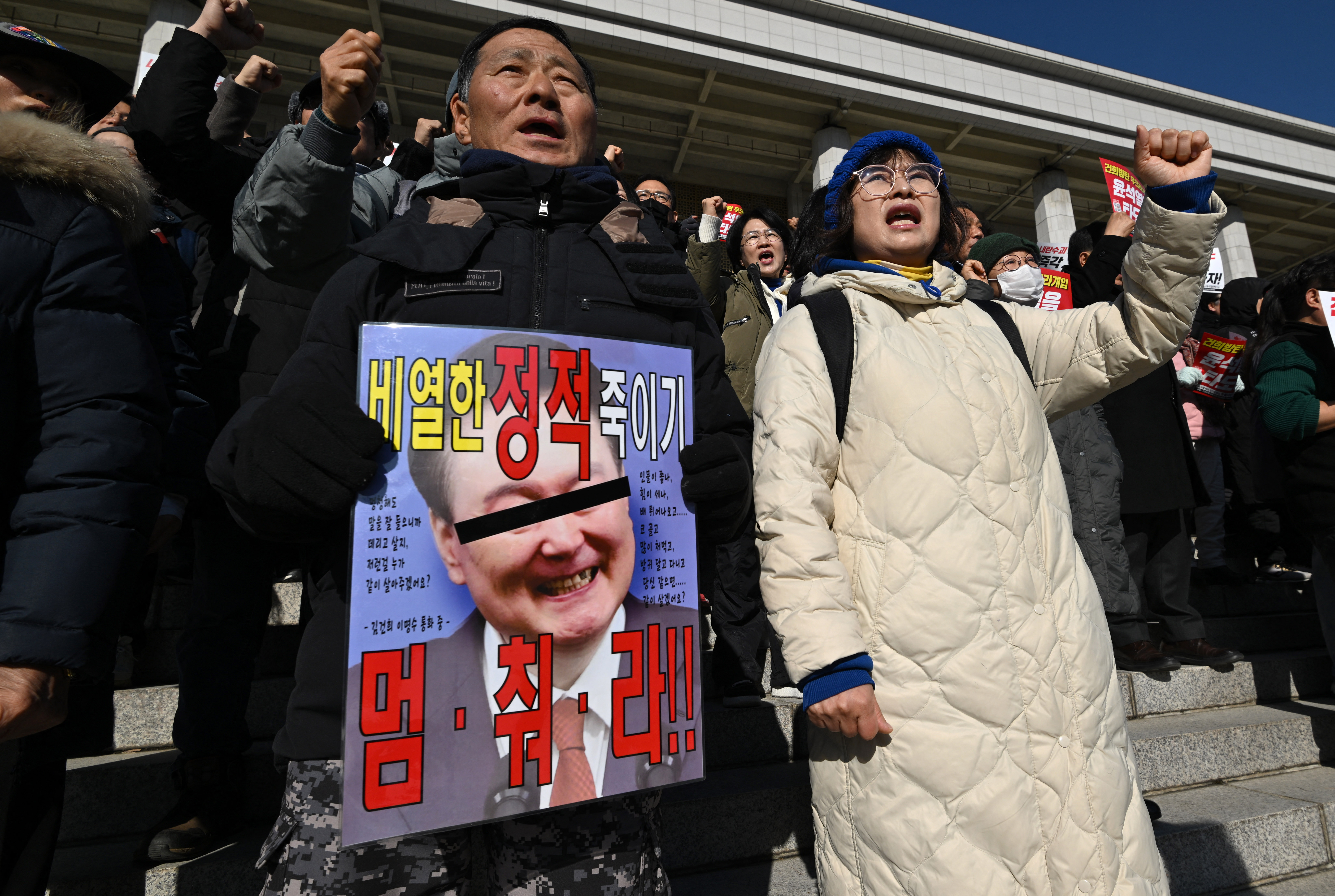 Members of South Korea's main opposition Democratic Party hold a placard showing a damaged picture of South Korean President Yoon Suk Yeol