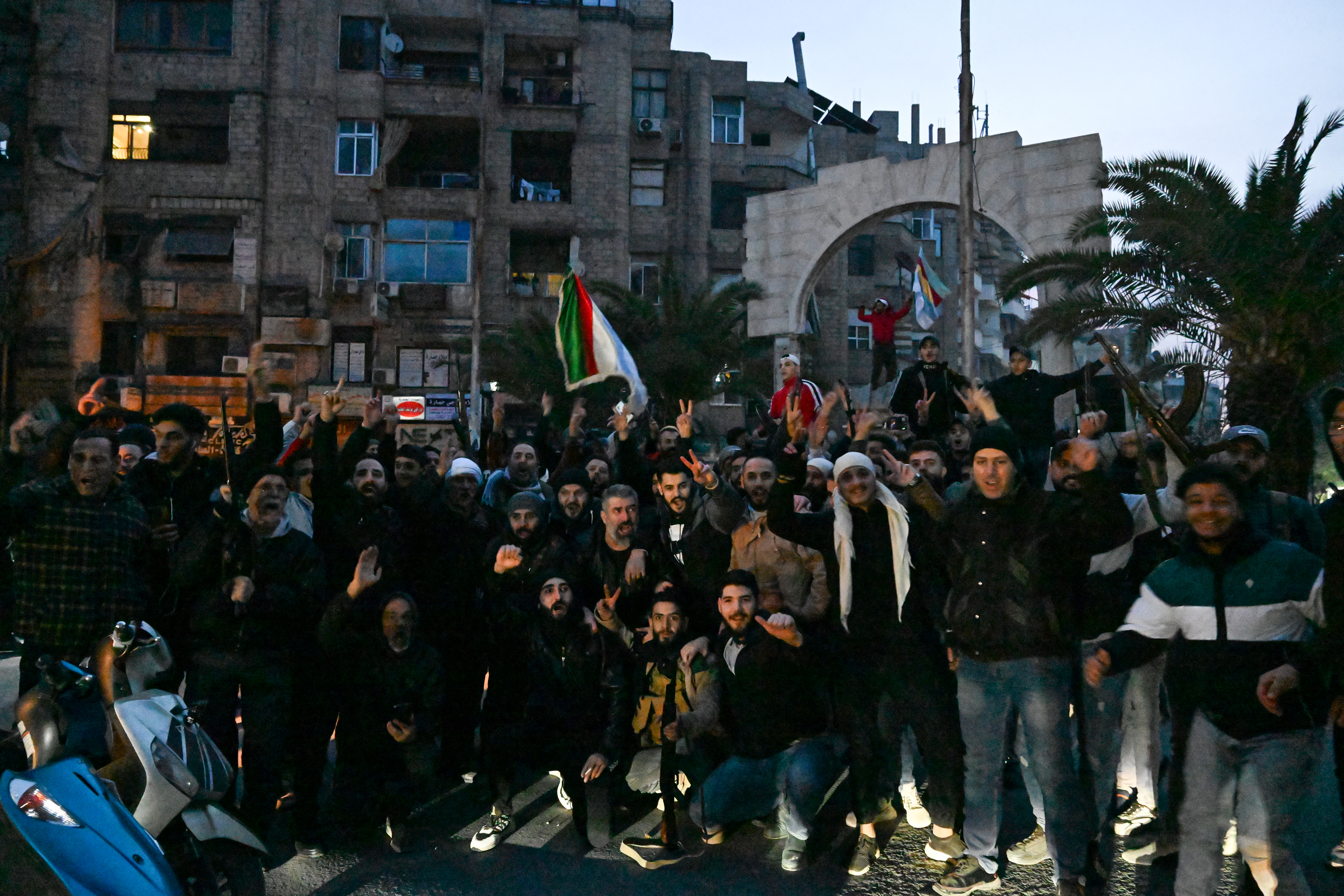a crowd of people with Syrian flags in front of an arch