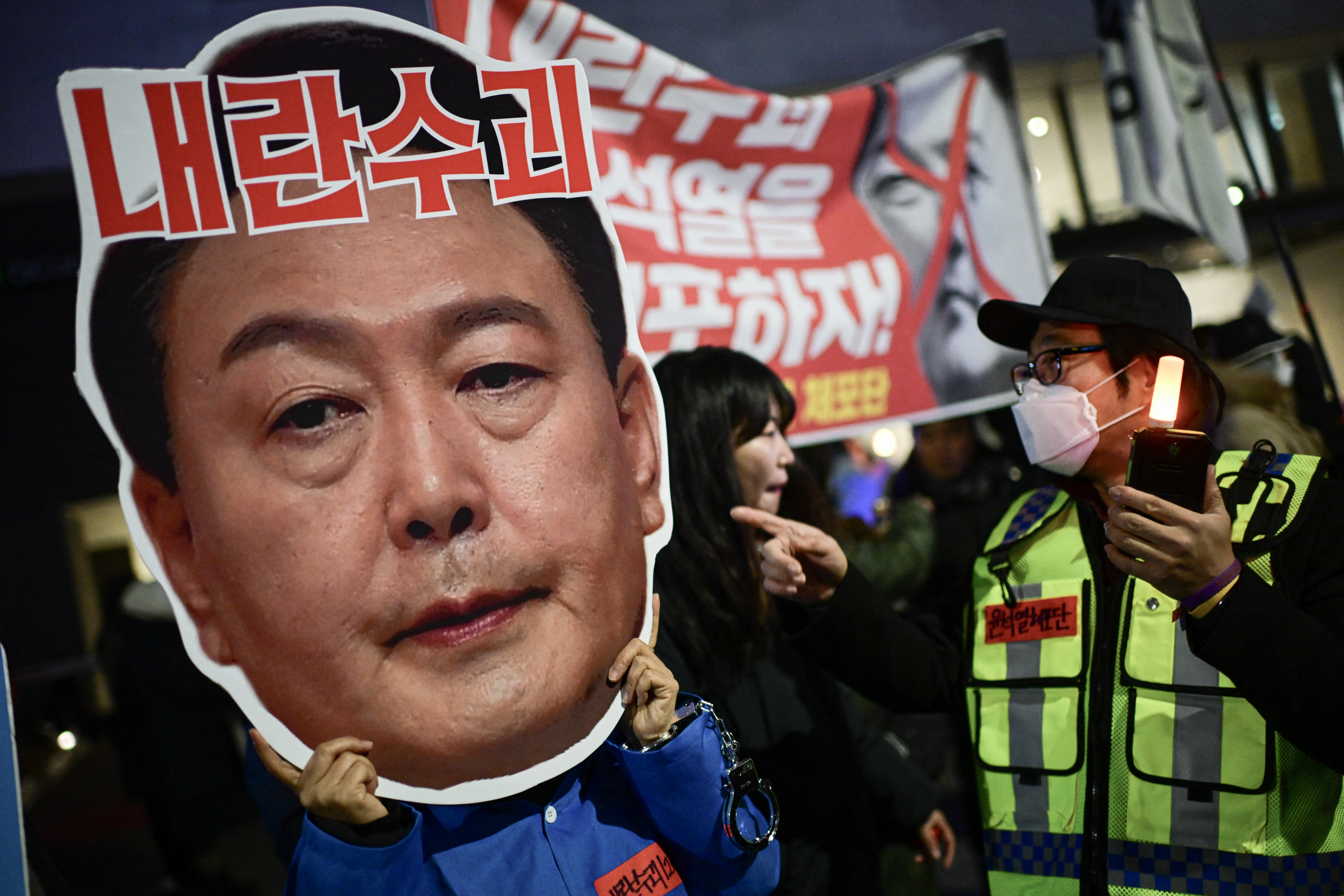 A protester holding a cardboard reading "Leader of insurgents" on an image depicting the face of South Korea's President Yoon Suk Yeol