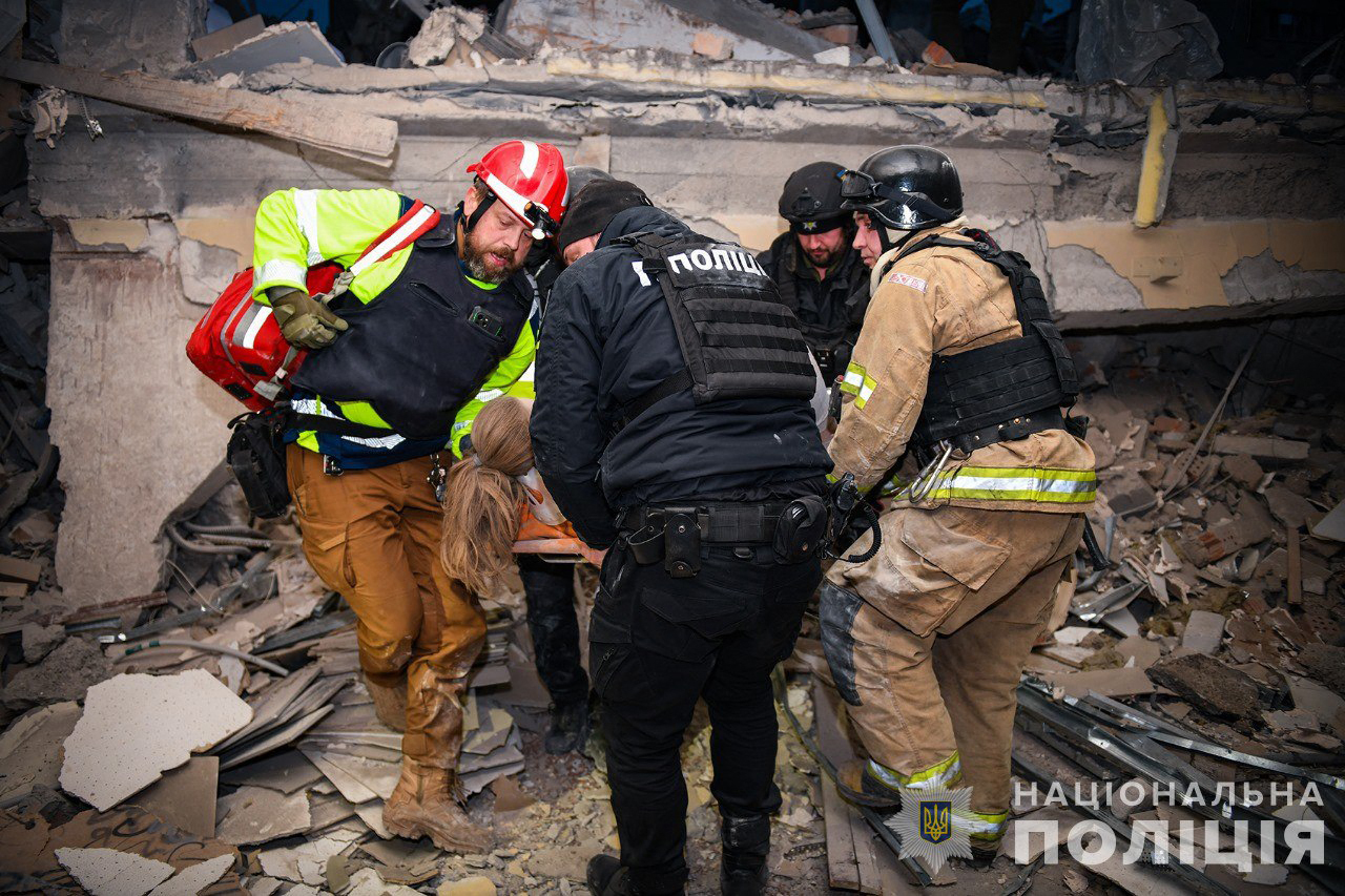 people carry a body out of a destroyed building