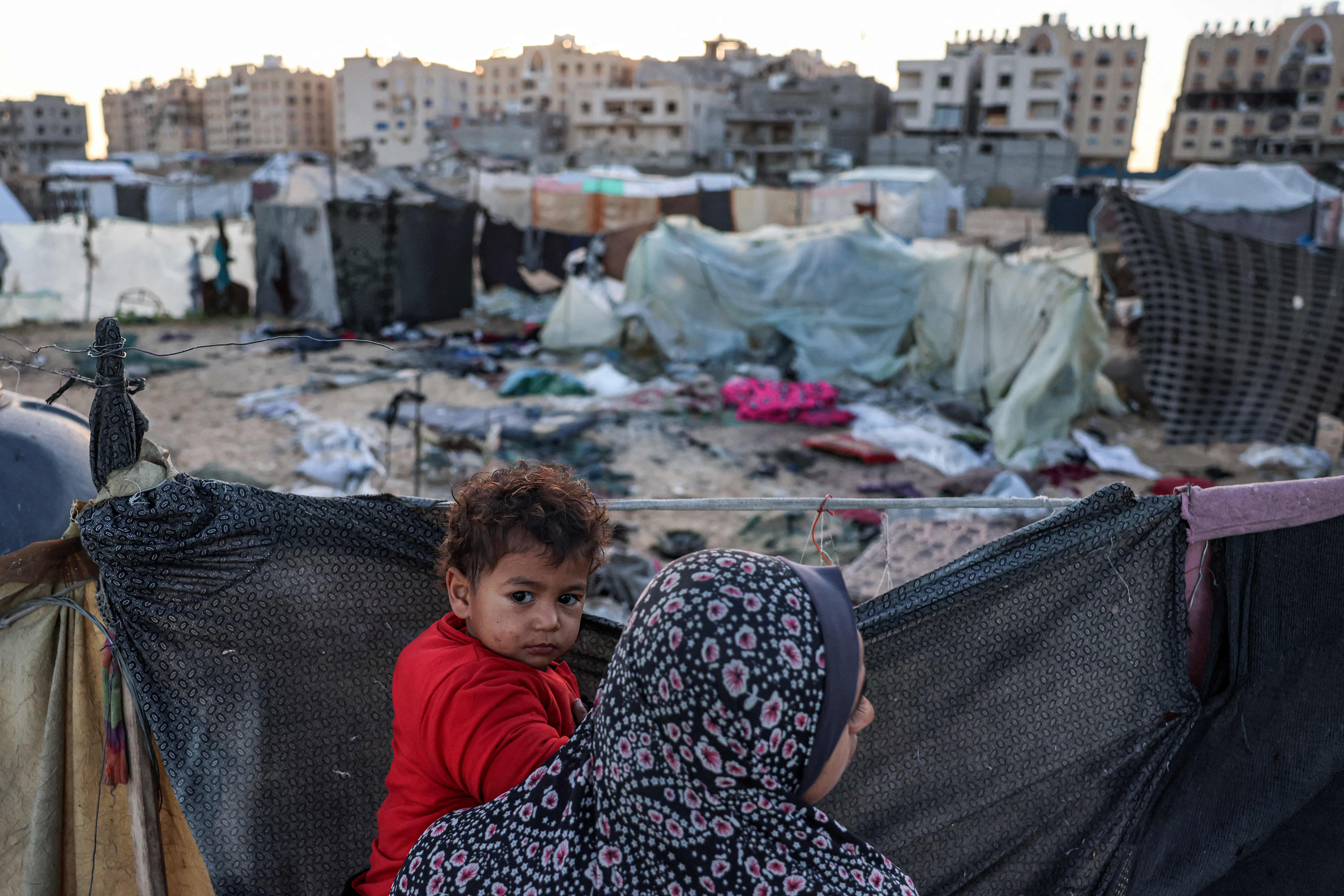 A woman holds a child near the site of reported Israeli bombardment on tents sheltering Palestinians displaced from Beit Lahia at a camp in Khan Younis