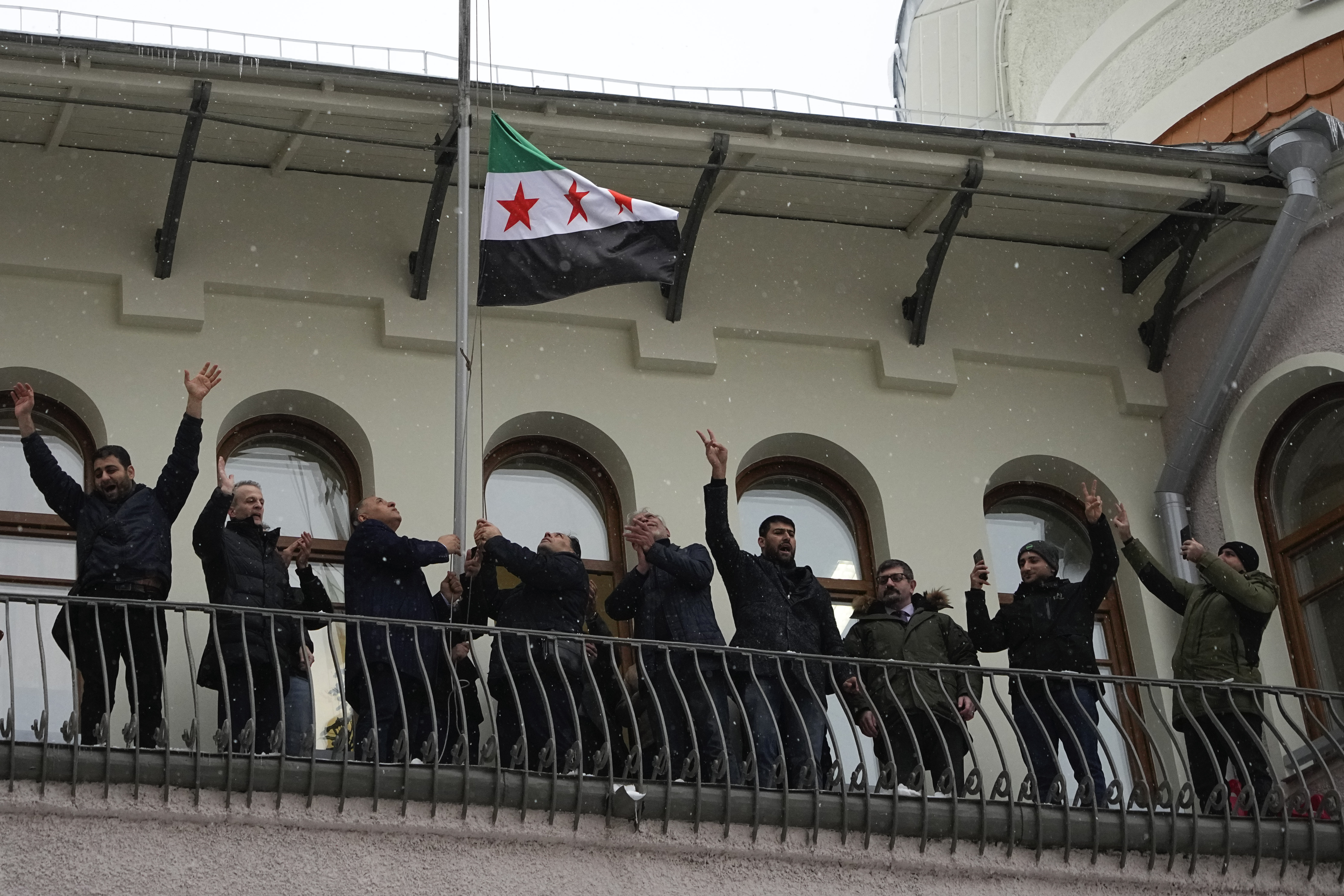 Members of the Syrian diaspora gesture while setting the Syrian opposition flag at the Syrian embassy, in Moscow