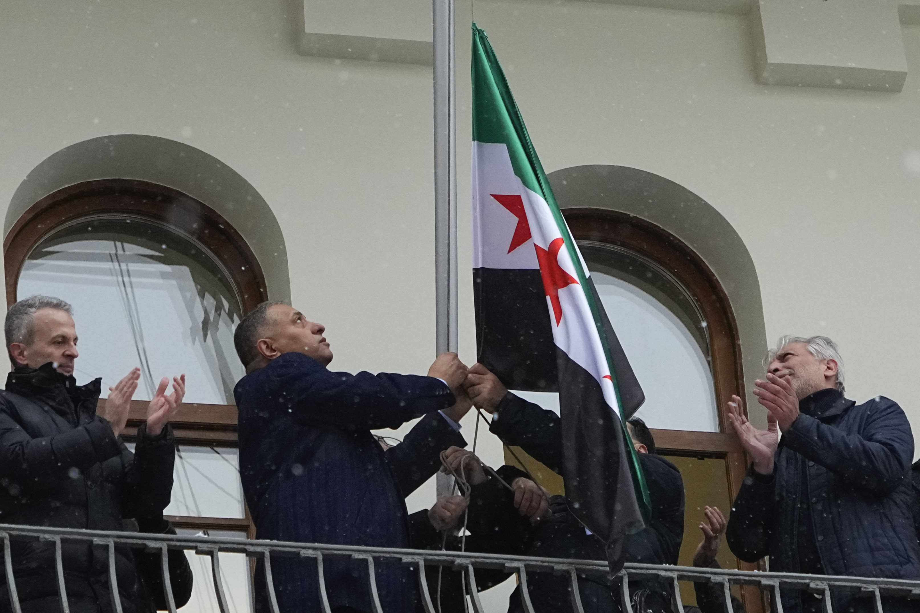 Members of the Syrian diaspora gesture while setting the Syrian opposition flag at the Syrian embassy, in Moscow