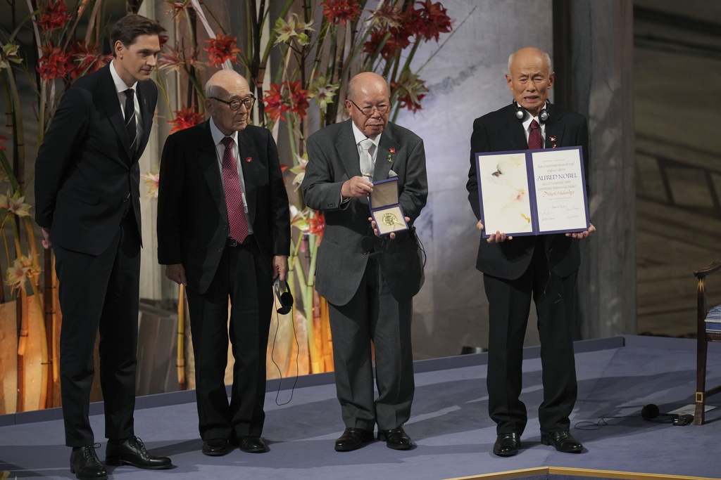 men in suits hold up a medal and a certificate in an ornatee hall