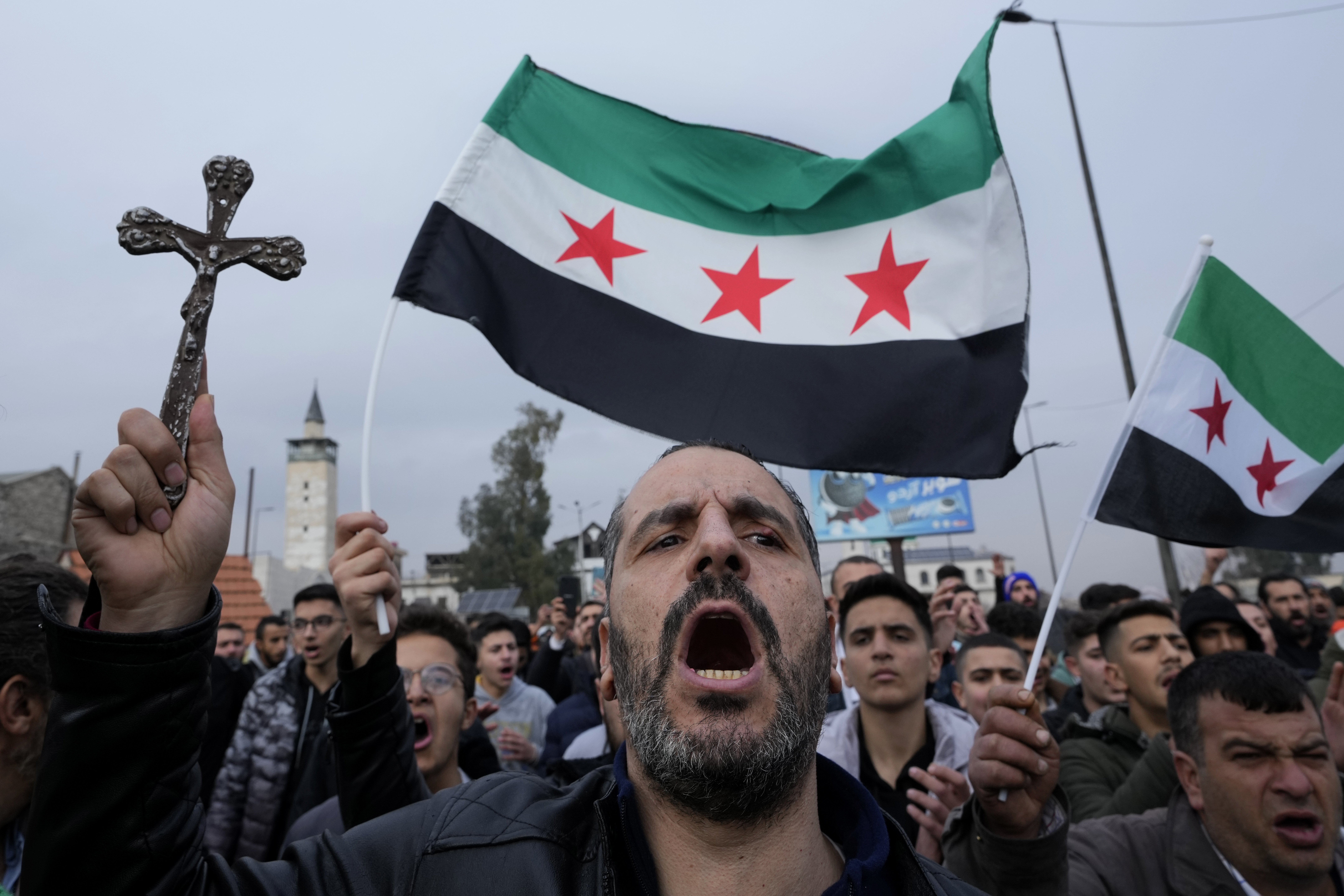 A Syrian Christian man holds up a cross and shouts slogans in Damascus