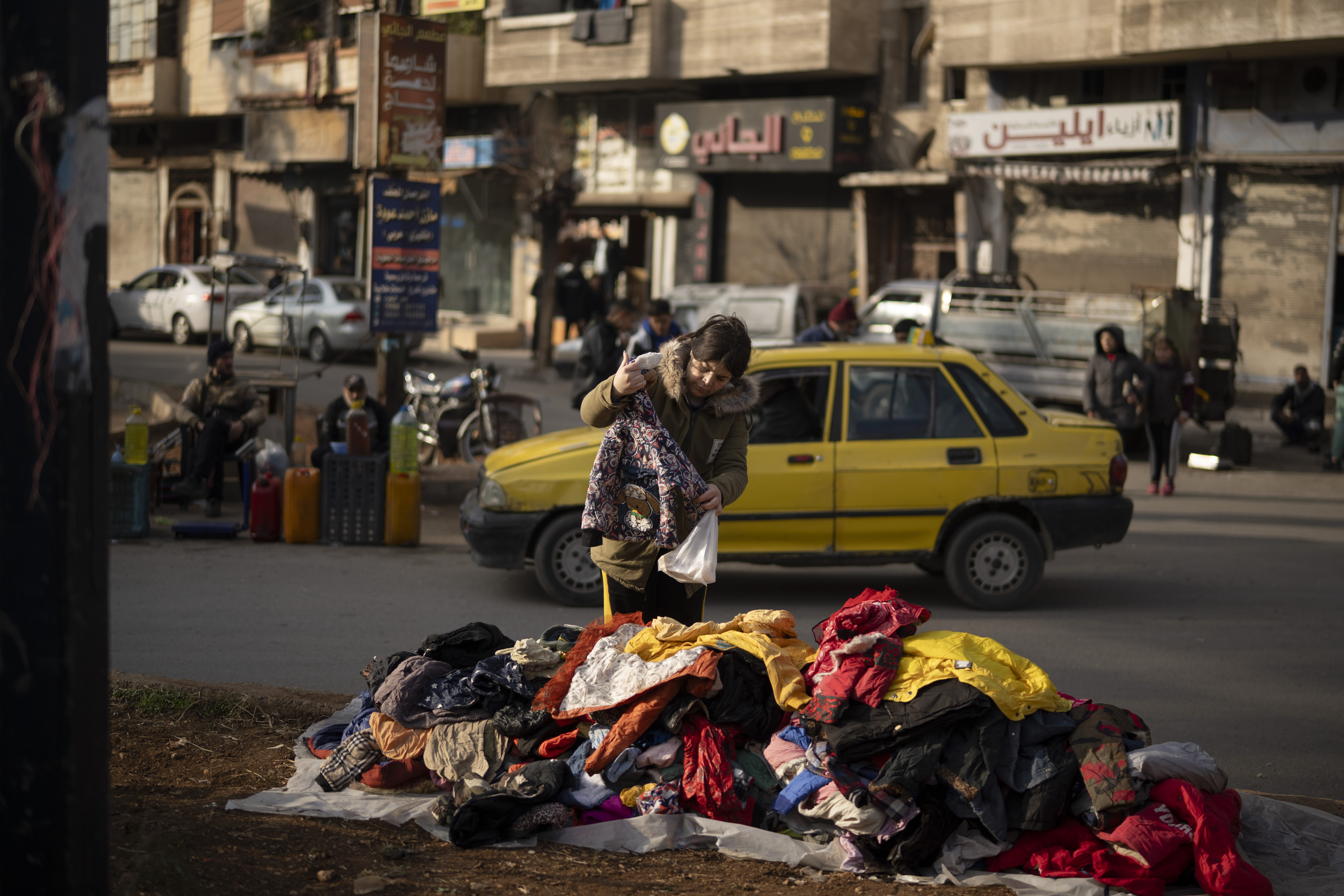 A women looks at second hand clothes displayed on a street for sale near an Alawite neighbourhood, in Homs, Syria, Thursday, Dec. 26