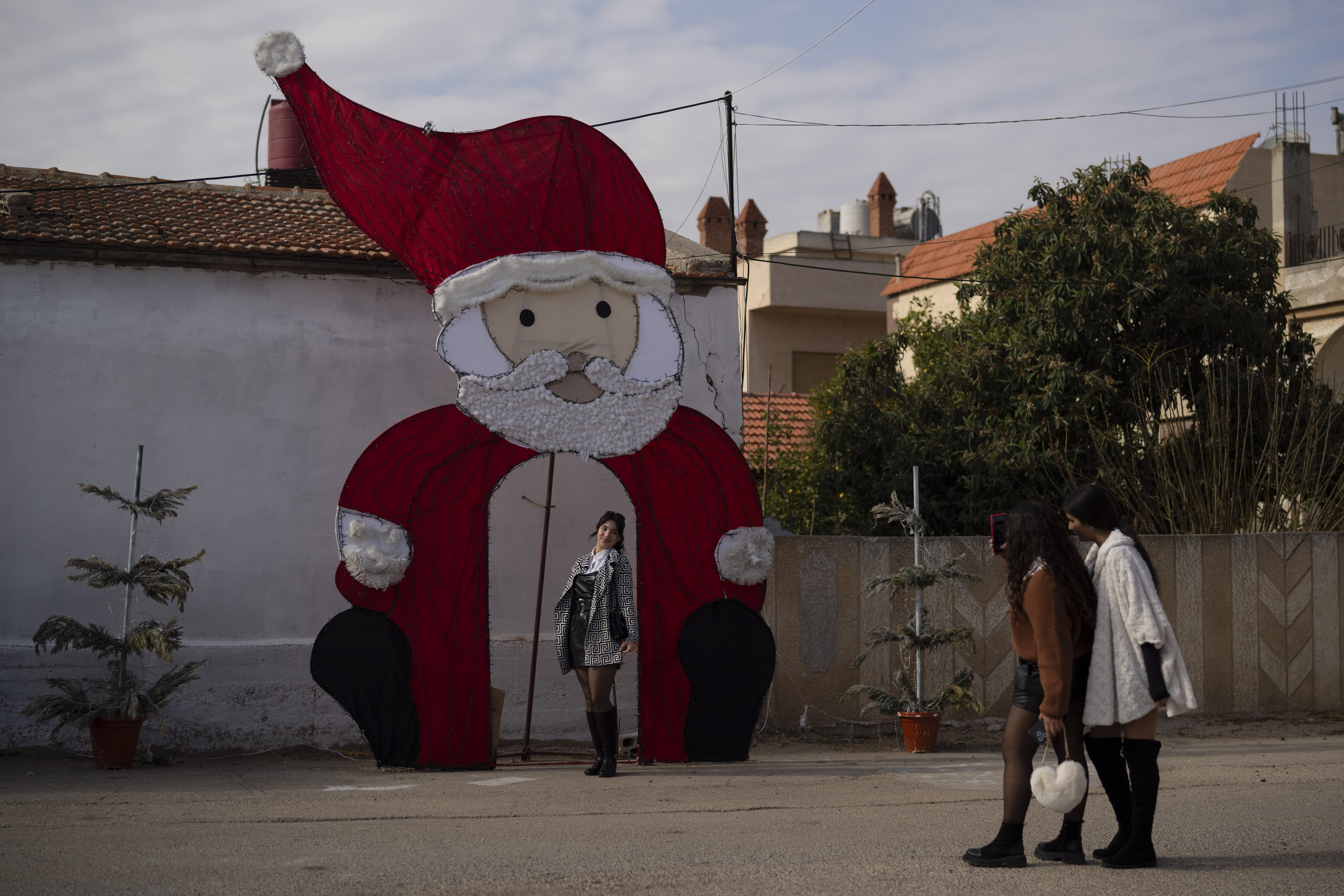 A young woman poses for a picture with a Christmas decoration on a square in a Christian neighbourhood, in Homs, Syria, Thursday, Dec. 26