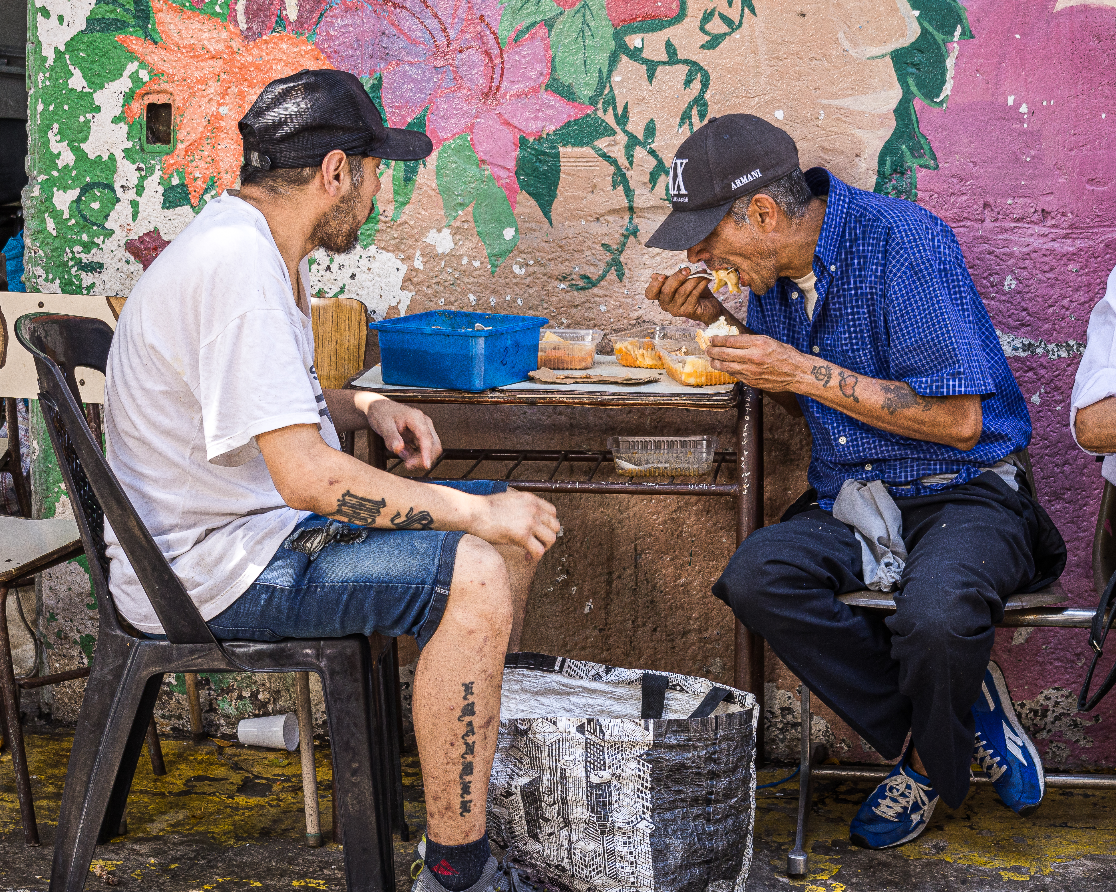 Two men sit at an outdoor table near a soup kitchen in Buenos Aires, Argentina.