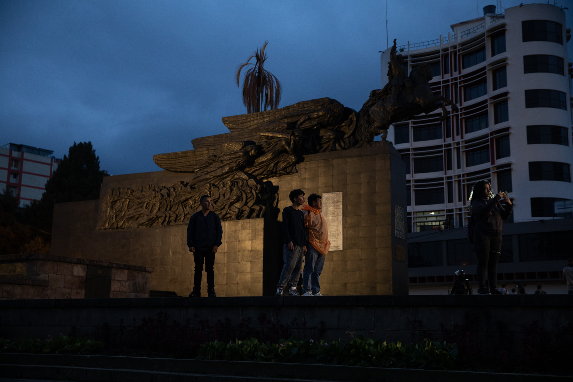 Protesters stand next to a statue in downtown Quito, as night falls with few lights due to widespread power outages