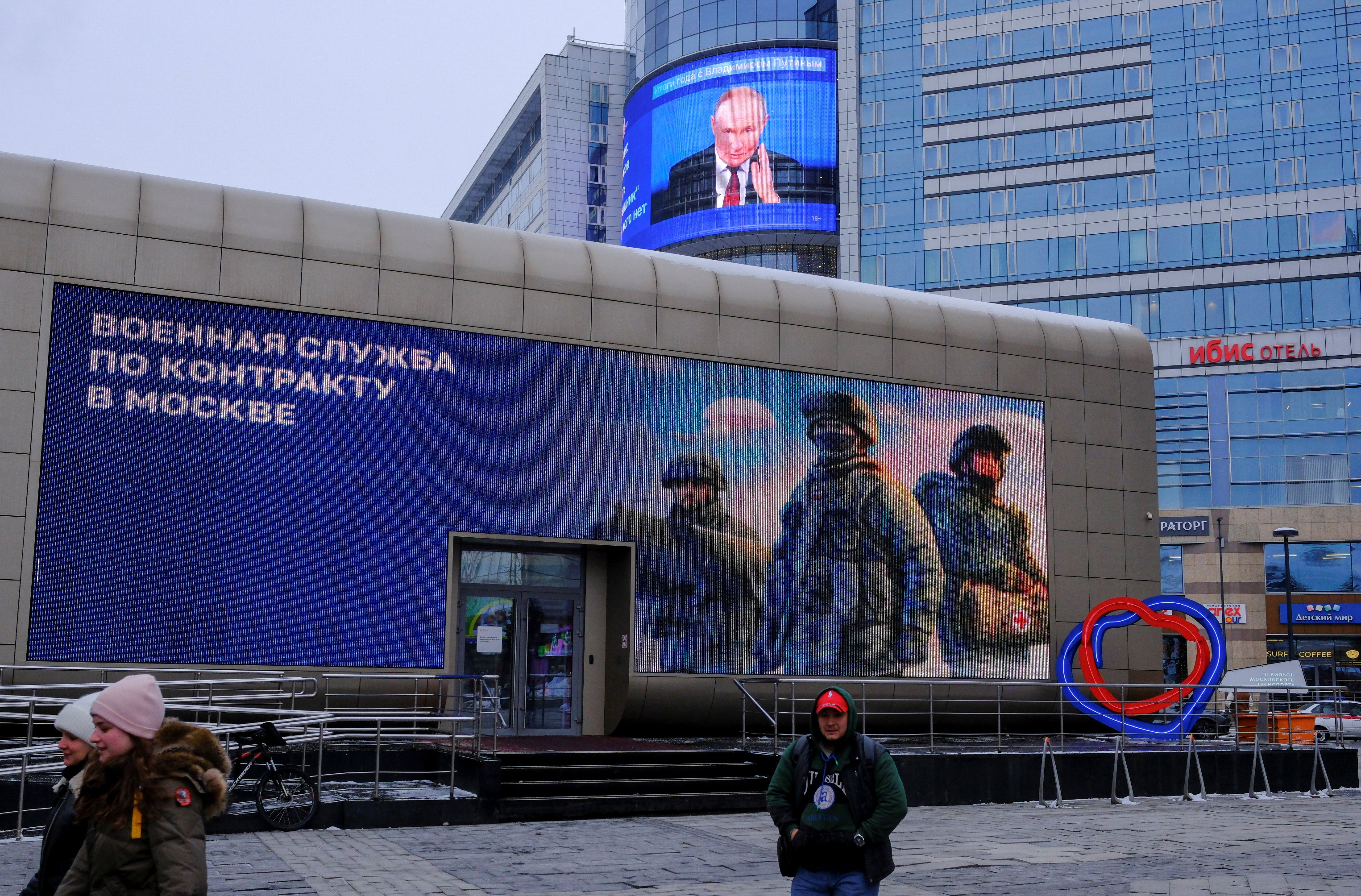 A screen, which shows an image of Russian President Vladimir Putin and a quote from his annual televised year-end press conference and phone-in, is on display on the facade of a building behind an electronic board promoting contract military service in the Russian army, in a street in Moscow, Russia December 19, 2024. REUTERS/Shamil Zhumatov