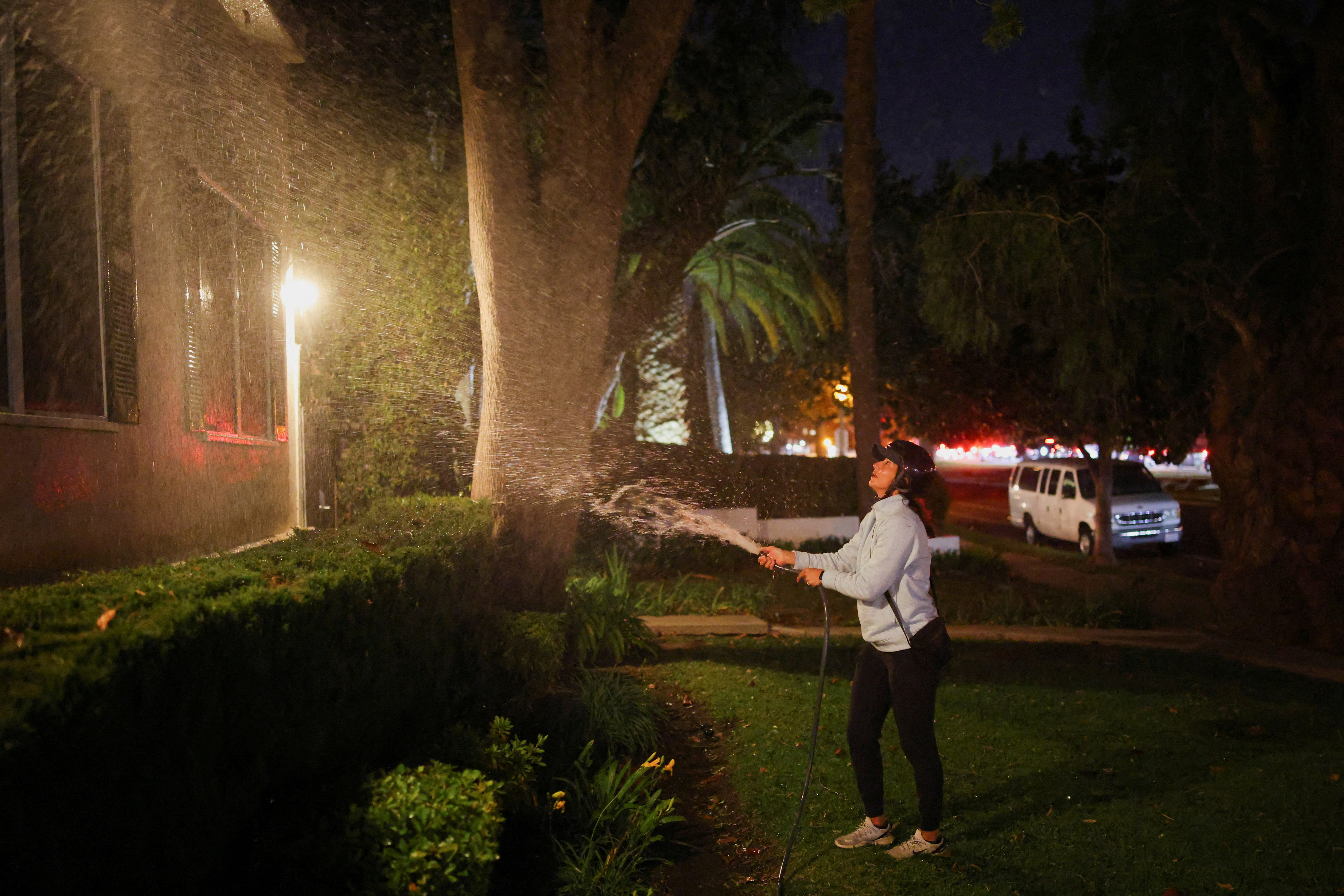 A woman waters the area in front of her house before leaving following an evacuation order, as a wildfire burns in the Pacific Palisades neighborhood of west Los Angeles, in Santa Monica, California, U.S., January 7