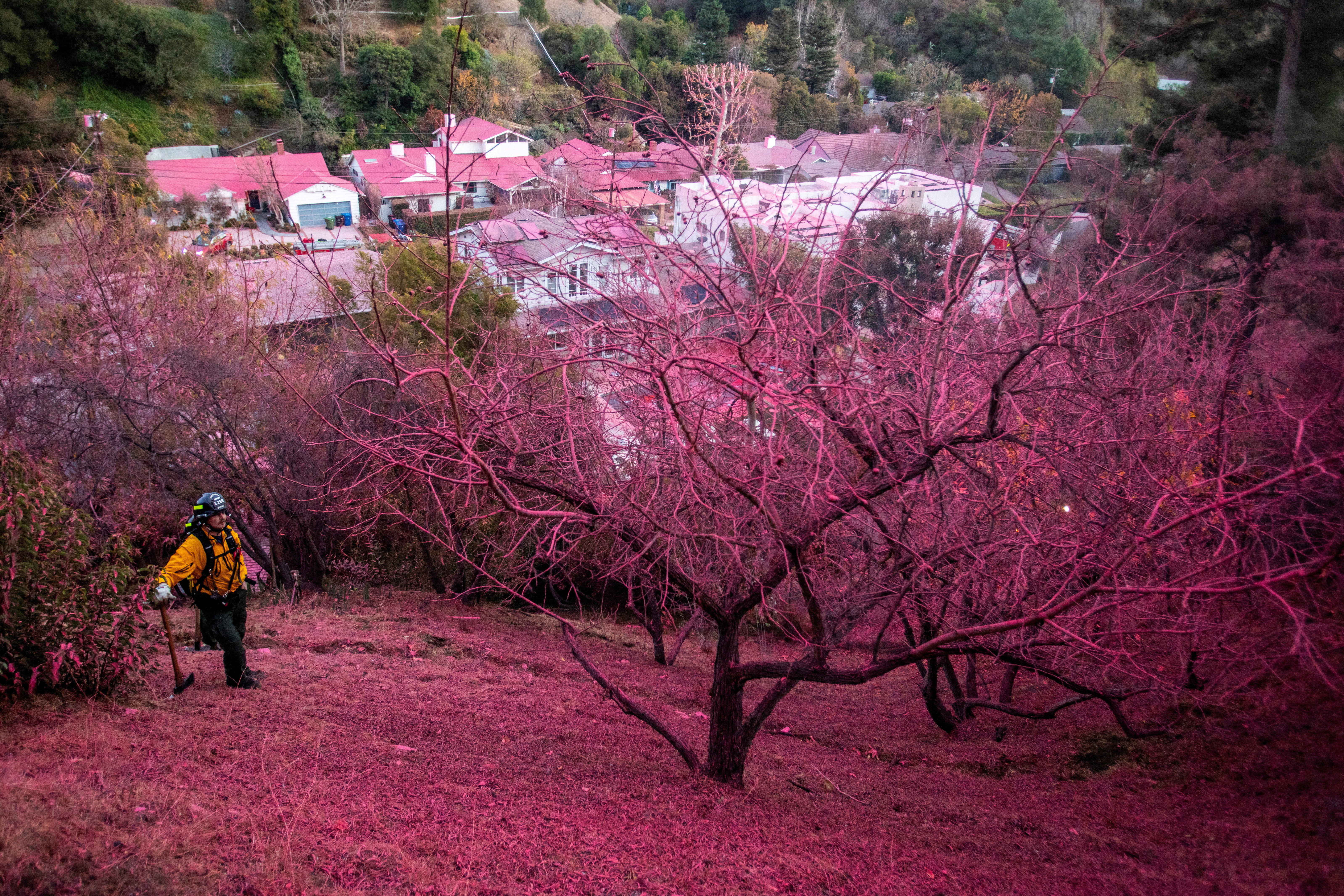 A firefighter stands on a hillside covered with retardant as the Palisades Fire, one of several simultaneous blazes that have ripped across Los Angeles County