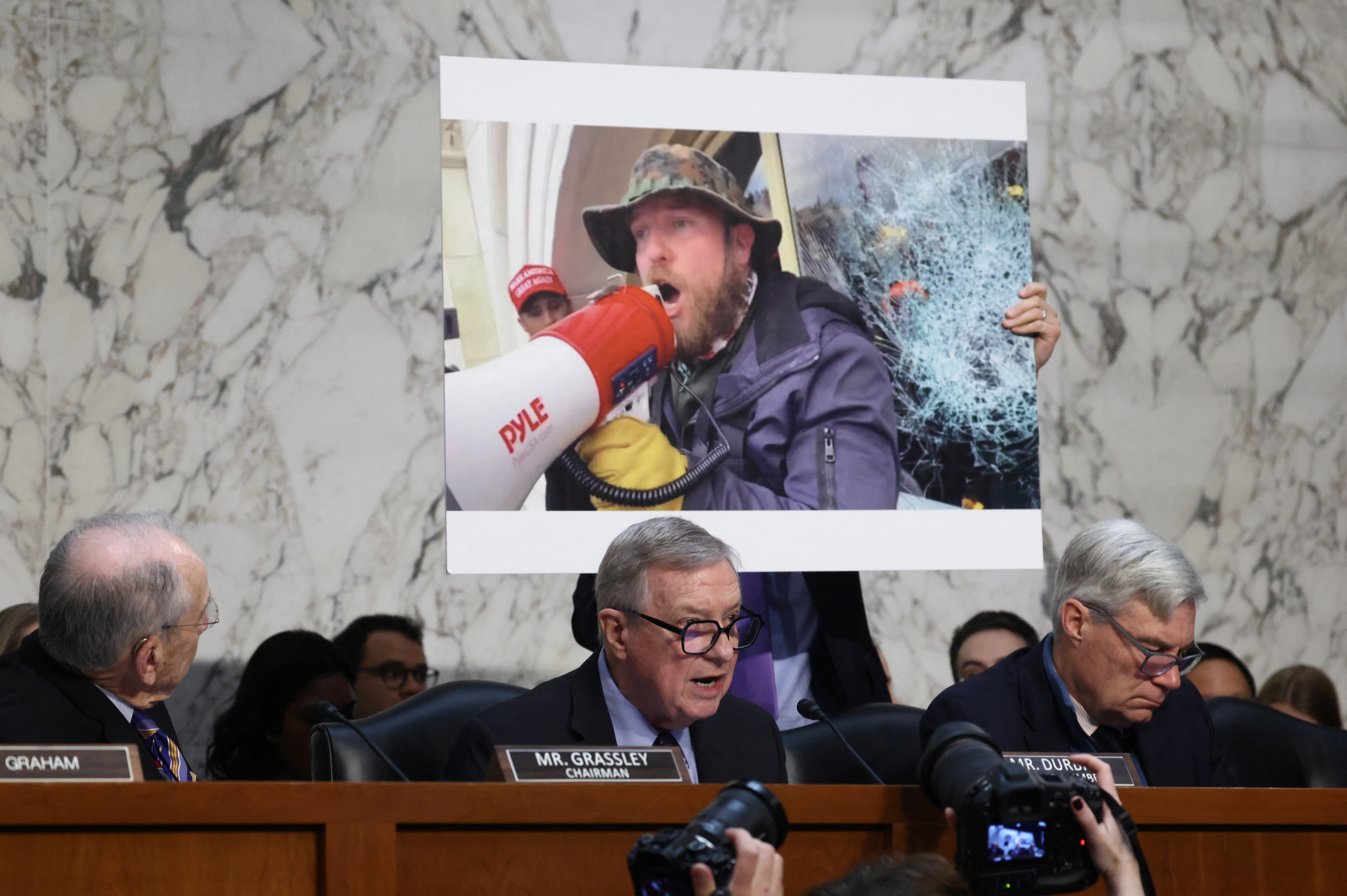 Dick Durbin speaks in front of an image of a January 6 rioter