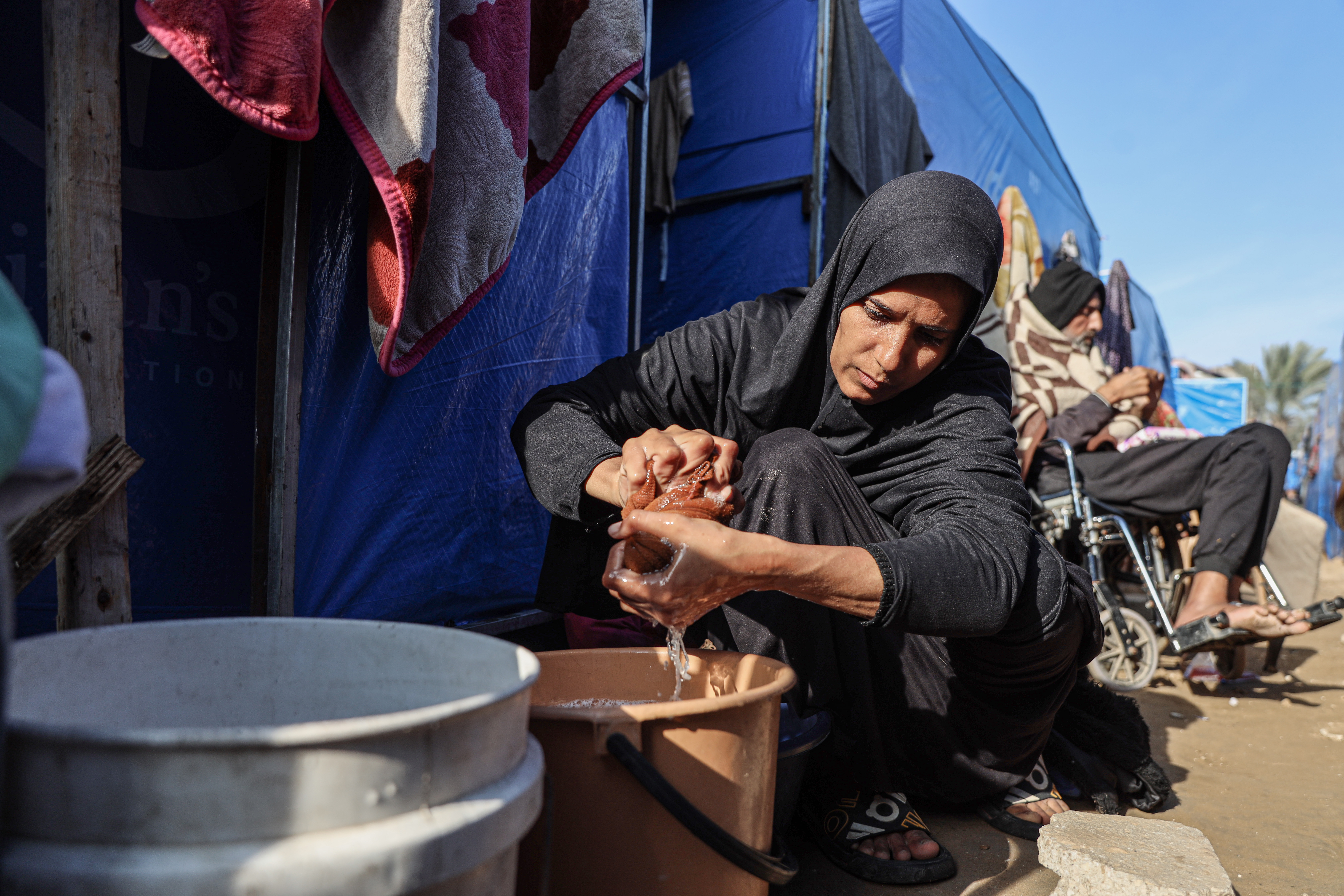 A woman squeezes water out of a sponge into a pot outside a tent