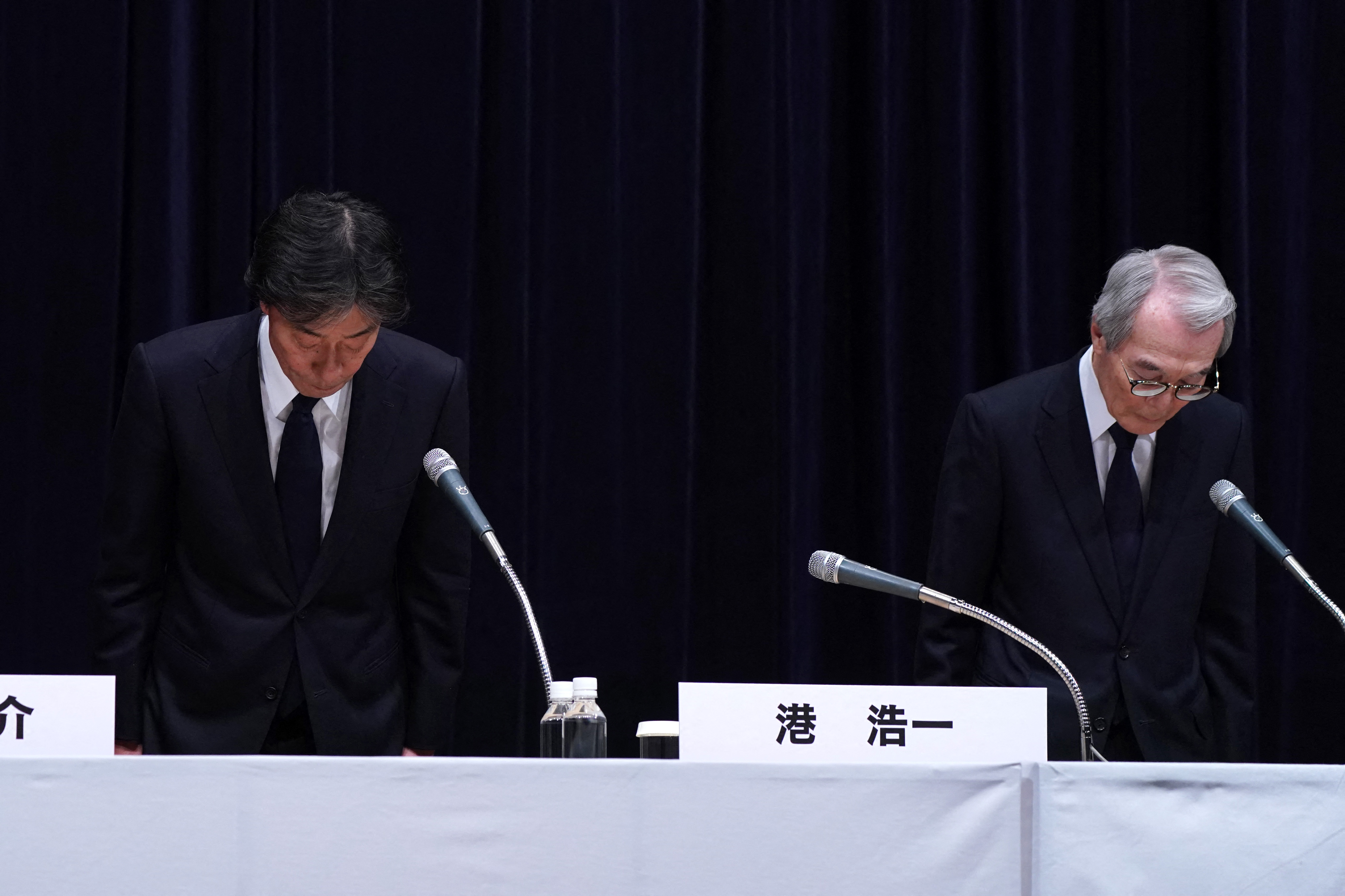 Koichi Minato (L) and Shuji Kano bow at the beginning of a news conference.
