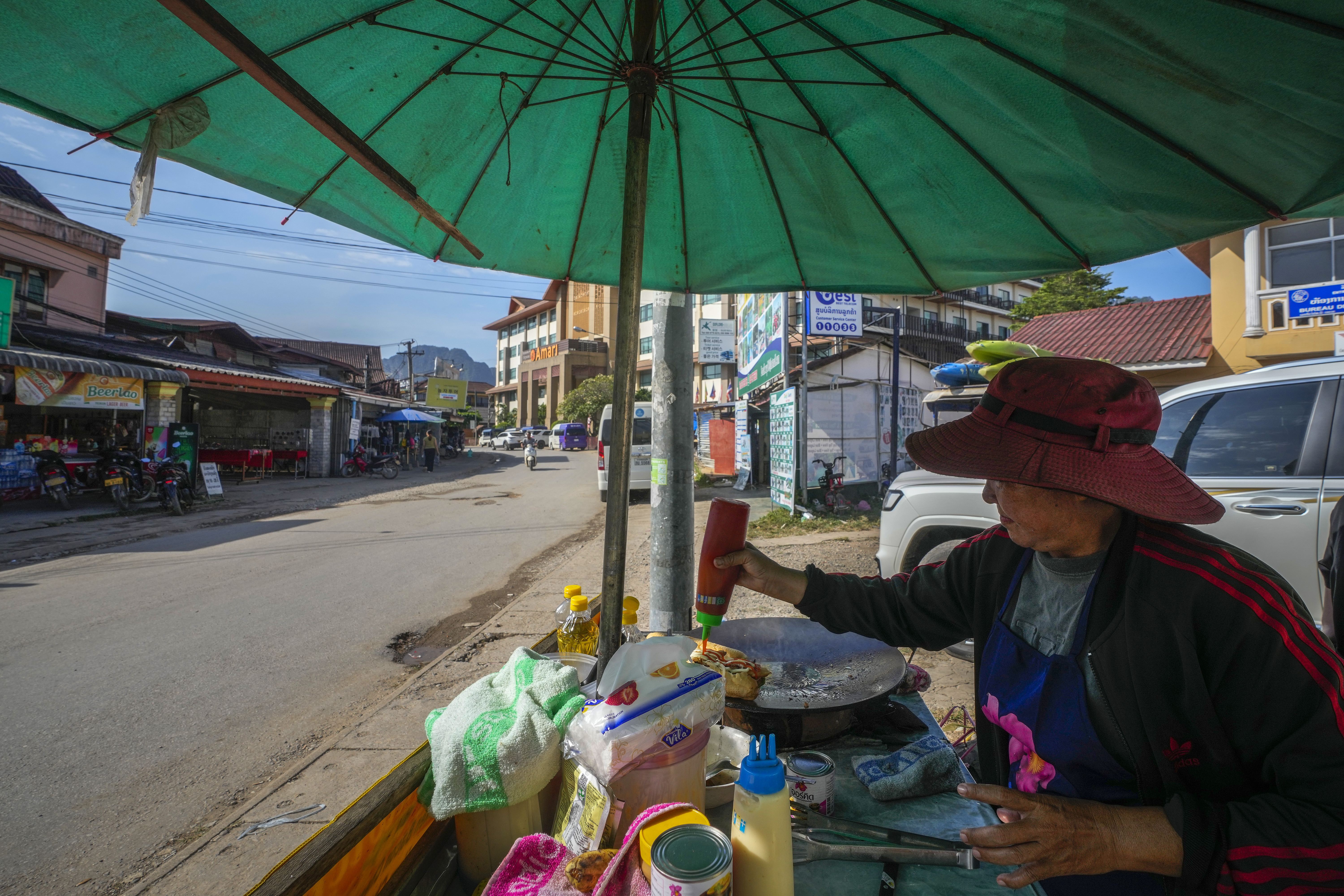 A local street woman vendor prepares food near an almost deserted road in Vang Vieng, Laos, Sunday, Nov. 24, 2024. (AP Photo/Anupam Nath)