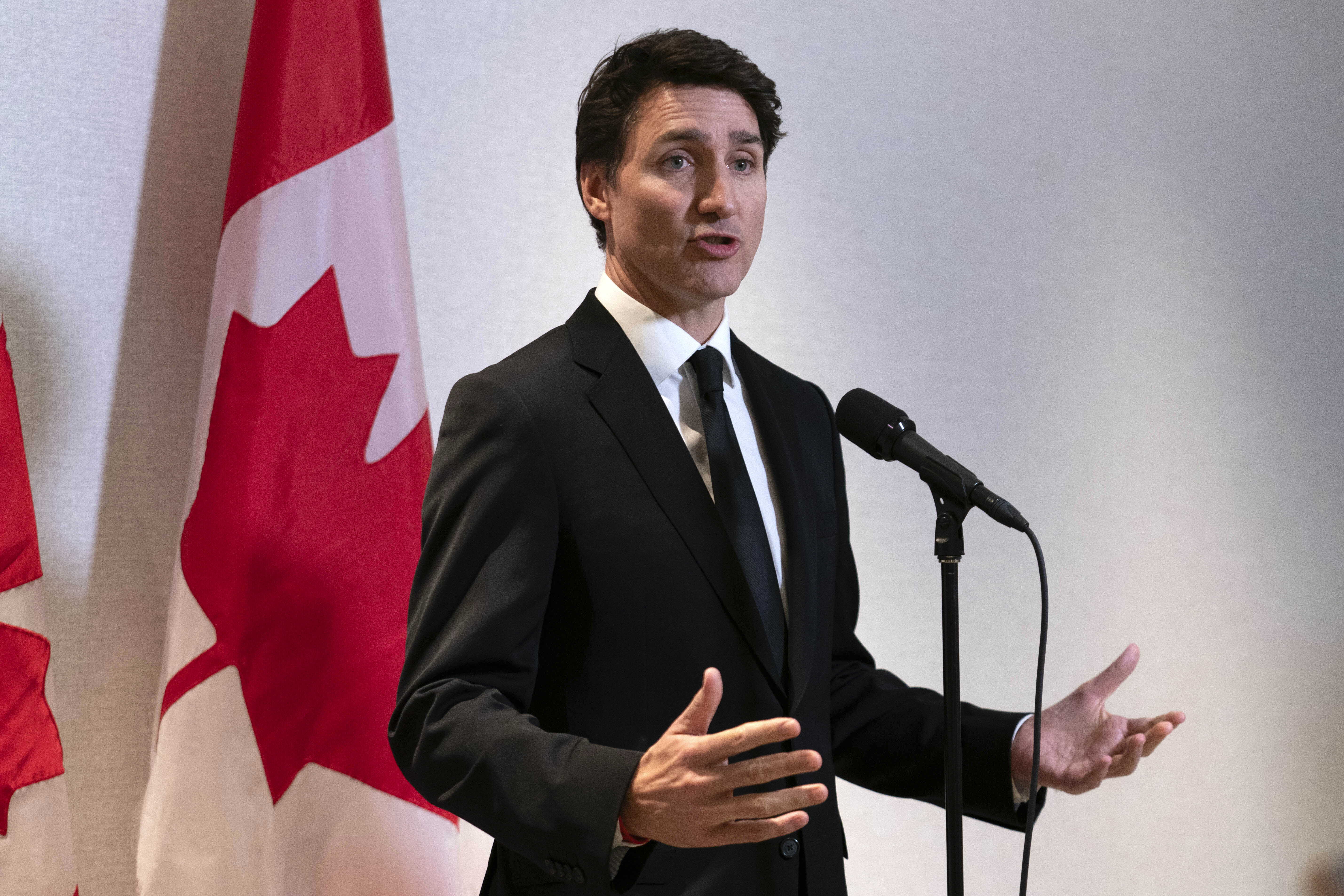 Justin Trudeau speaks at a microphone in front of a Canadian flag.