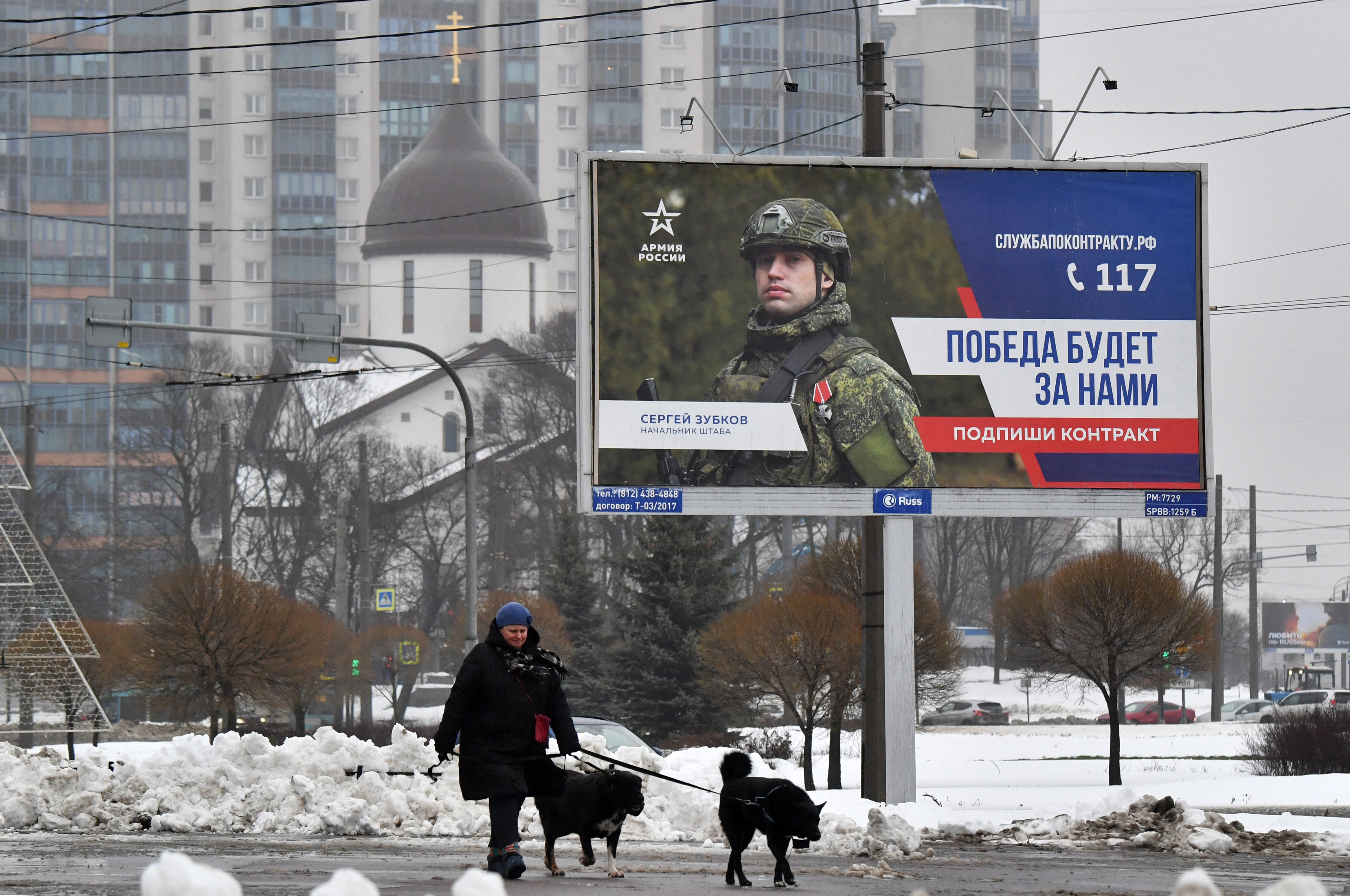 A woman walks dogs past a billboard promoting contract army service with the slogan "The Victory will be ours" in Saint Petersburg on January 14, 2025. (Photo by Olga MALTSEVA / AFP)
