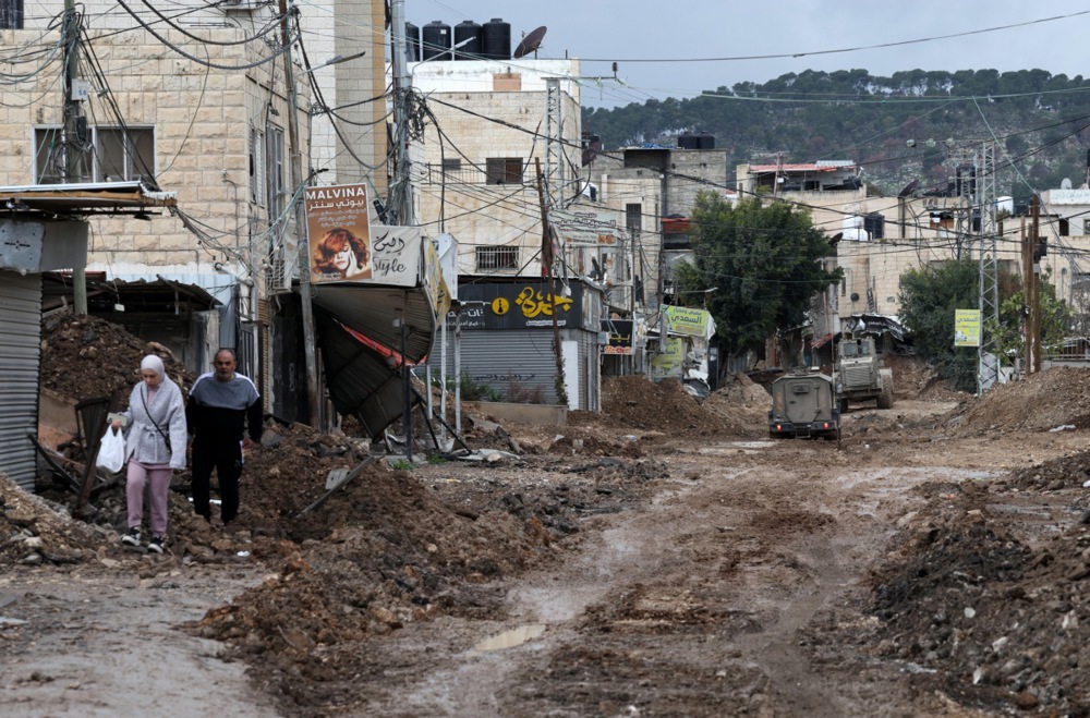 Palestinians walk along a damaged road near the main entrance to Jenin refugee camp