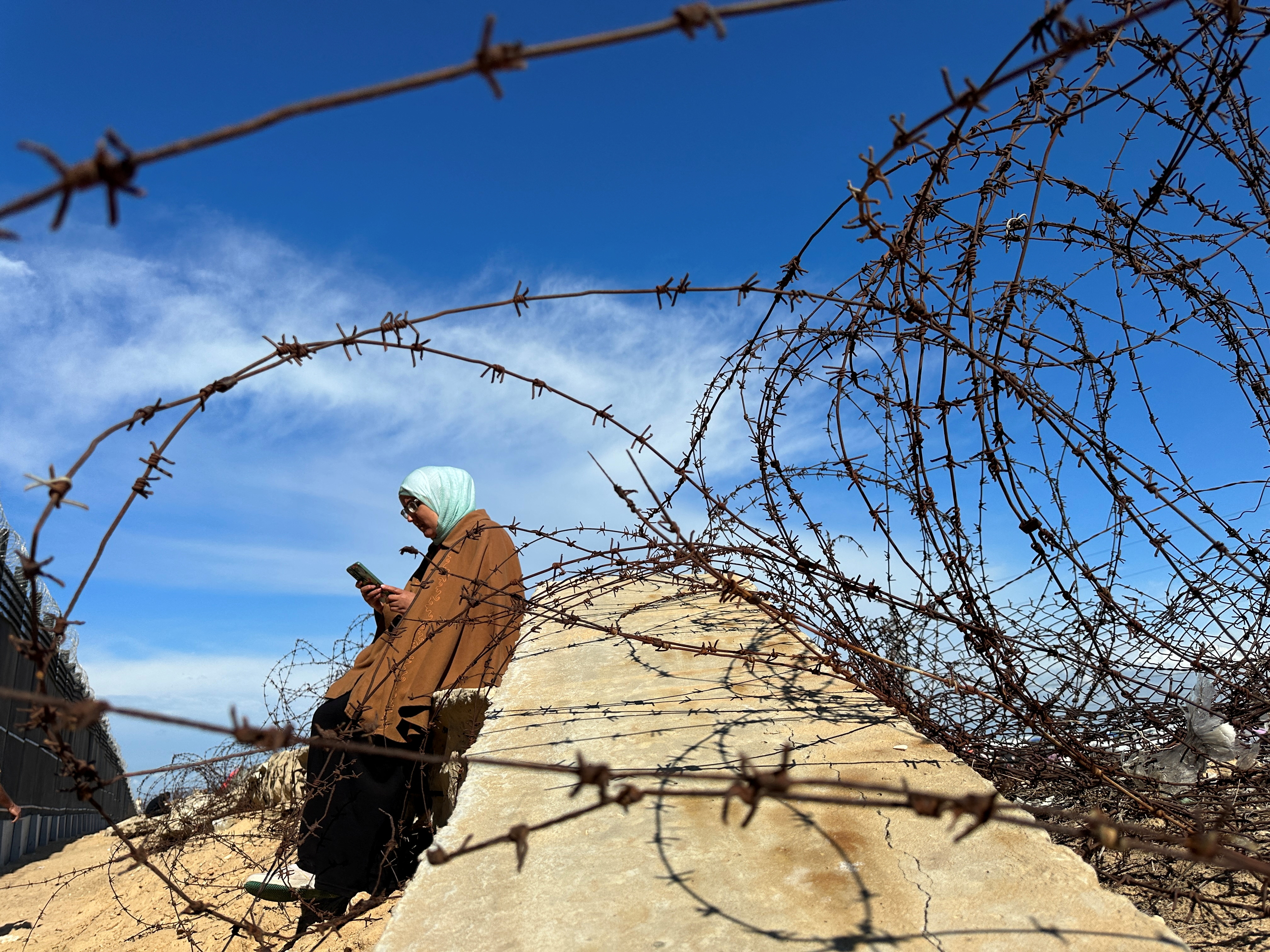 A displaced Palestinian woman tries to get internet service on her phone through the Egyptian networks to communicate with her relatives, near the border with Egypt, in Rafah in the southern Gaza Strip February 1, 2024. REUTERS/Mohammed Salem