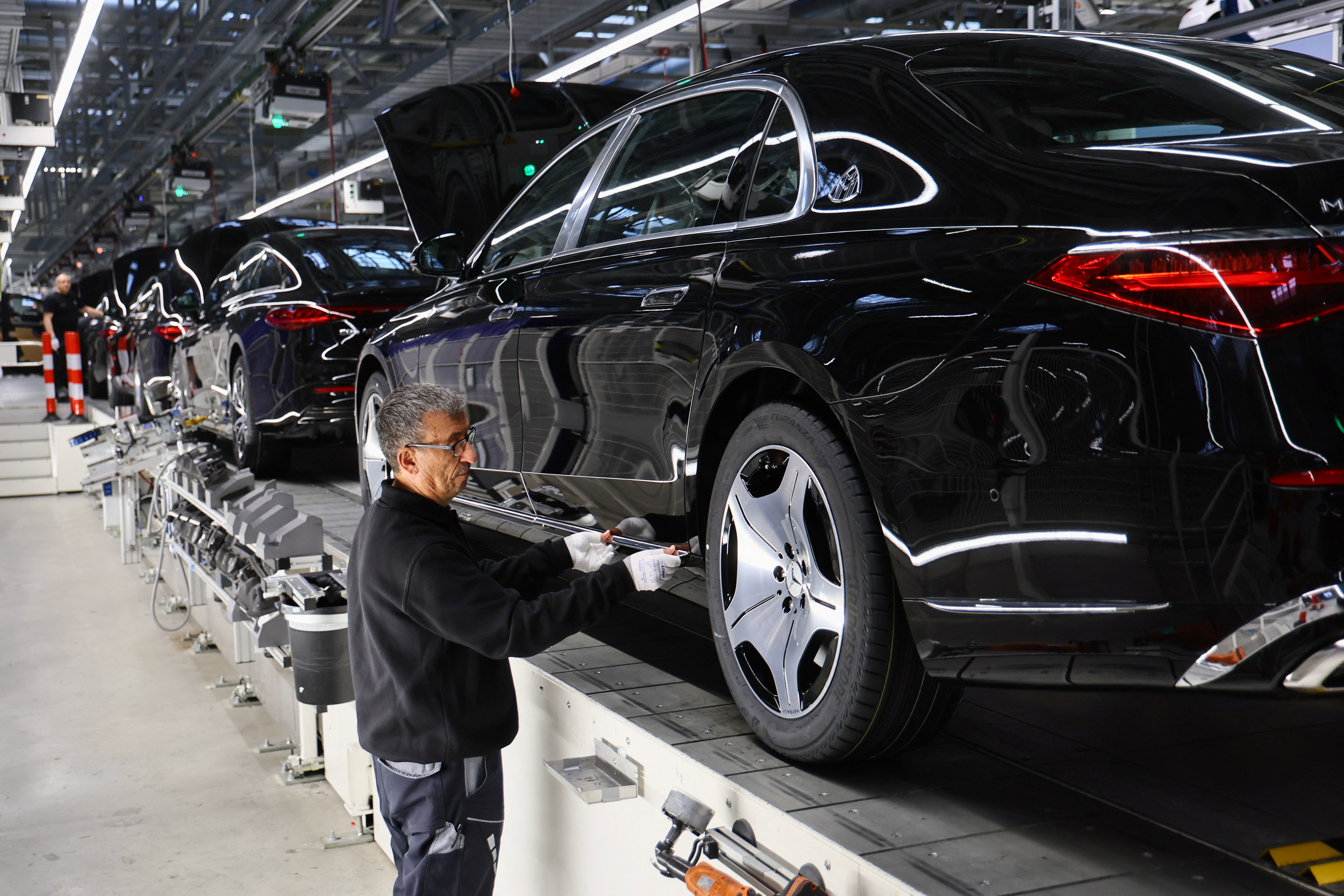 A worker attaches a part to a Mercedes-Maybach car on a production line [File: Wolfgang Rattay/Reuters]
