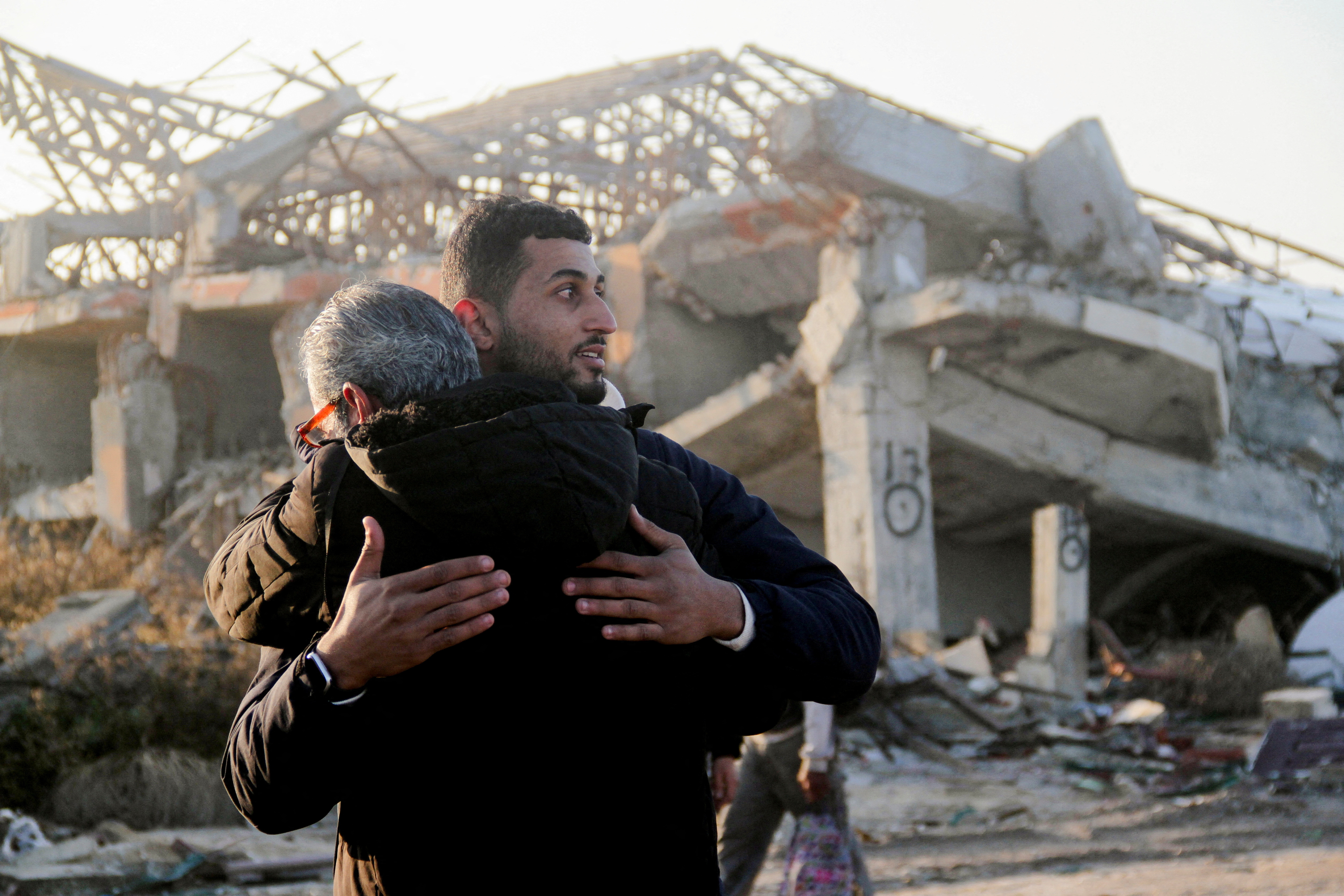 Two Palestinians hug in front of a destroyed building