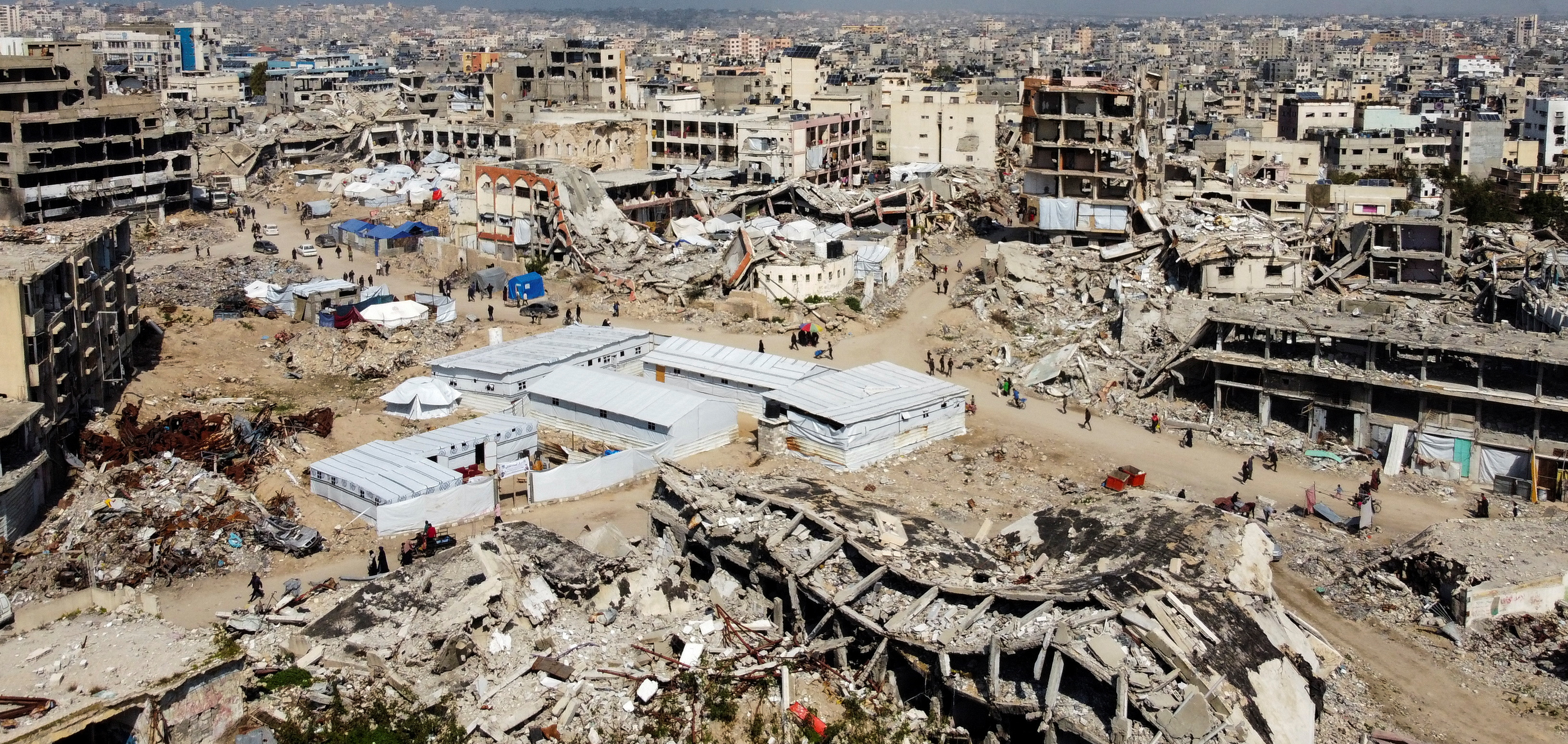 A drone view shows Palestinians walking past buildings damaged and destroyed during the Israeli offensive