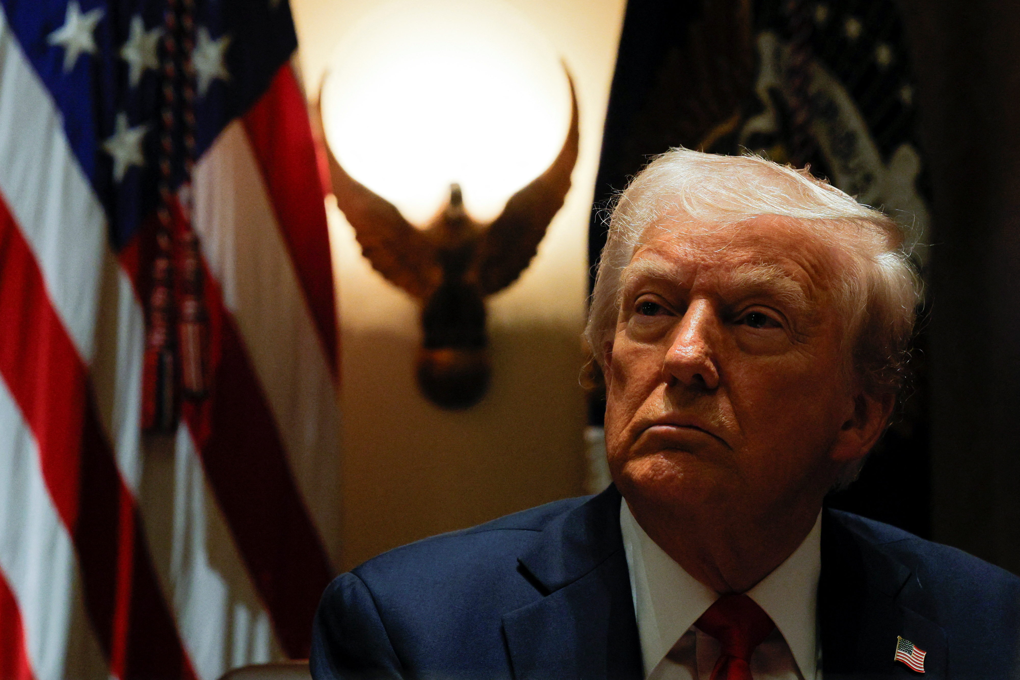 Donald Trump looks up at a cabinet meeting. Behind him is a light silhouetted by an eagle.