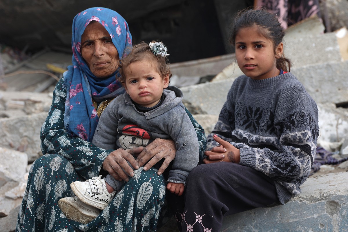 A Palestinian woman and children sit amid the rubble