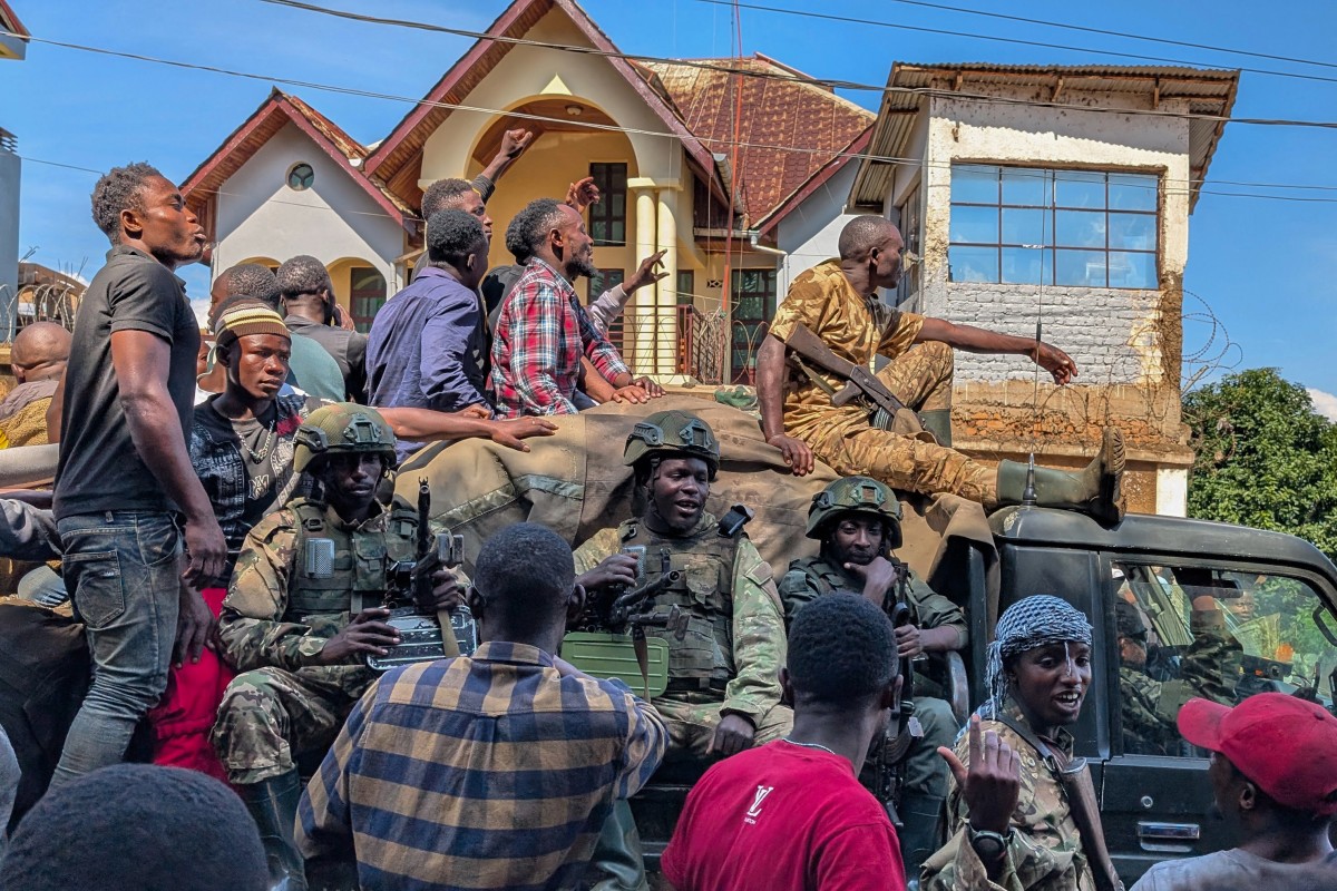 Residents walk next to a vehicle with M23 fighters on in Bukavu
