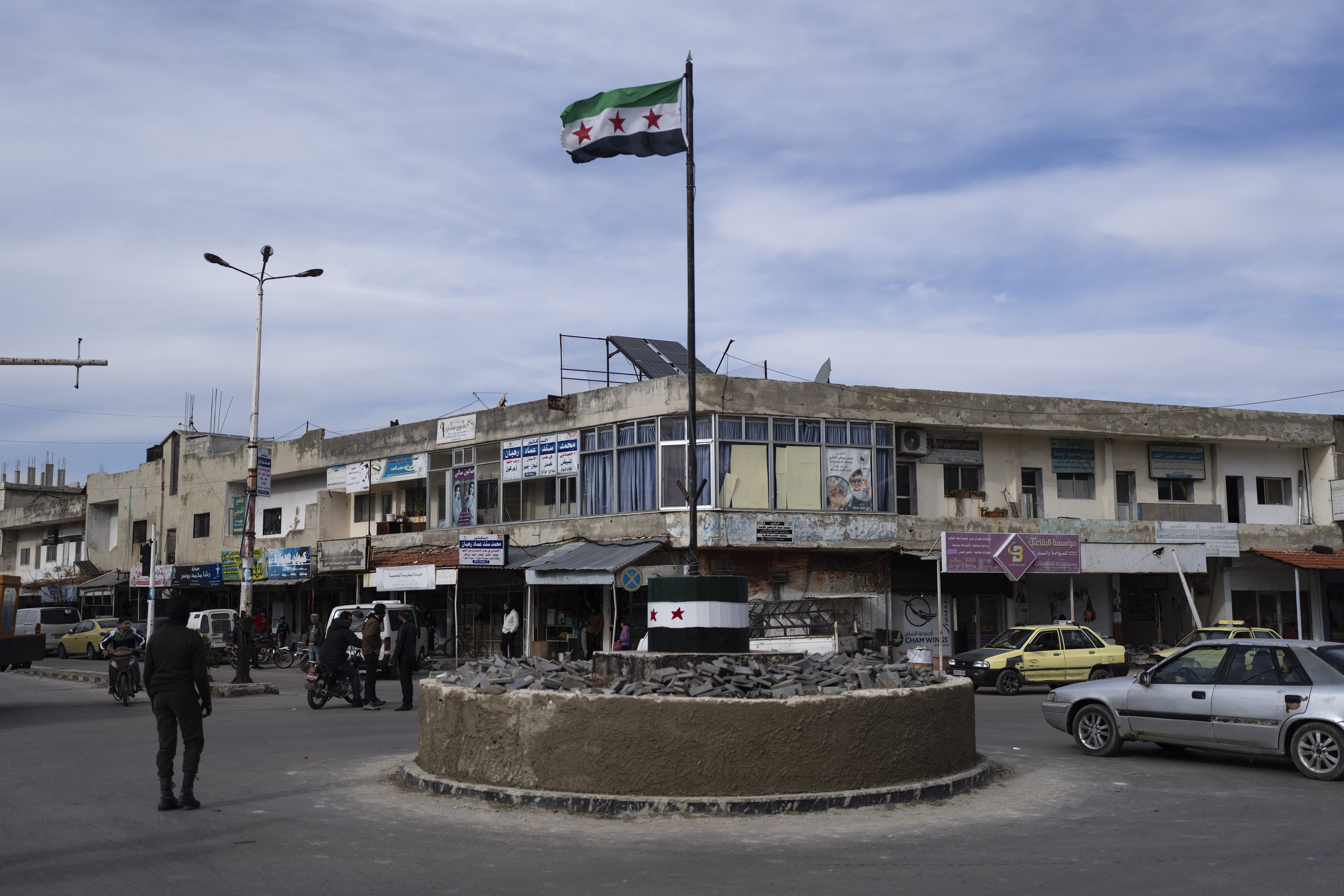 Cars drive past a roundabout hoisting the new Syrian flag after the ousting of the Assad regime
