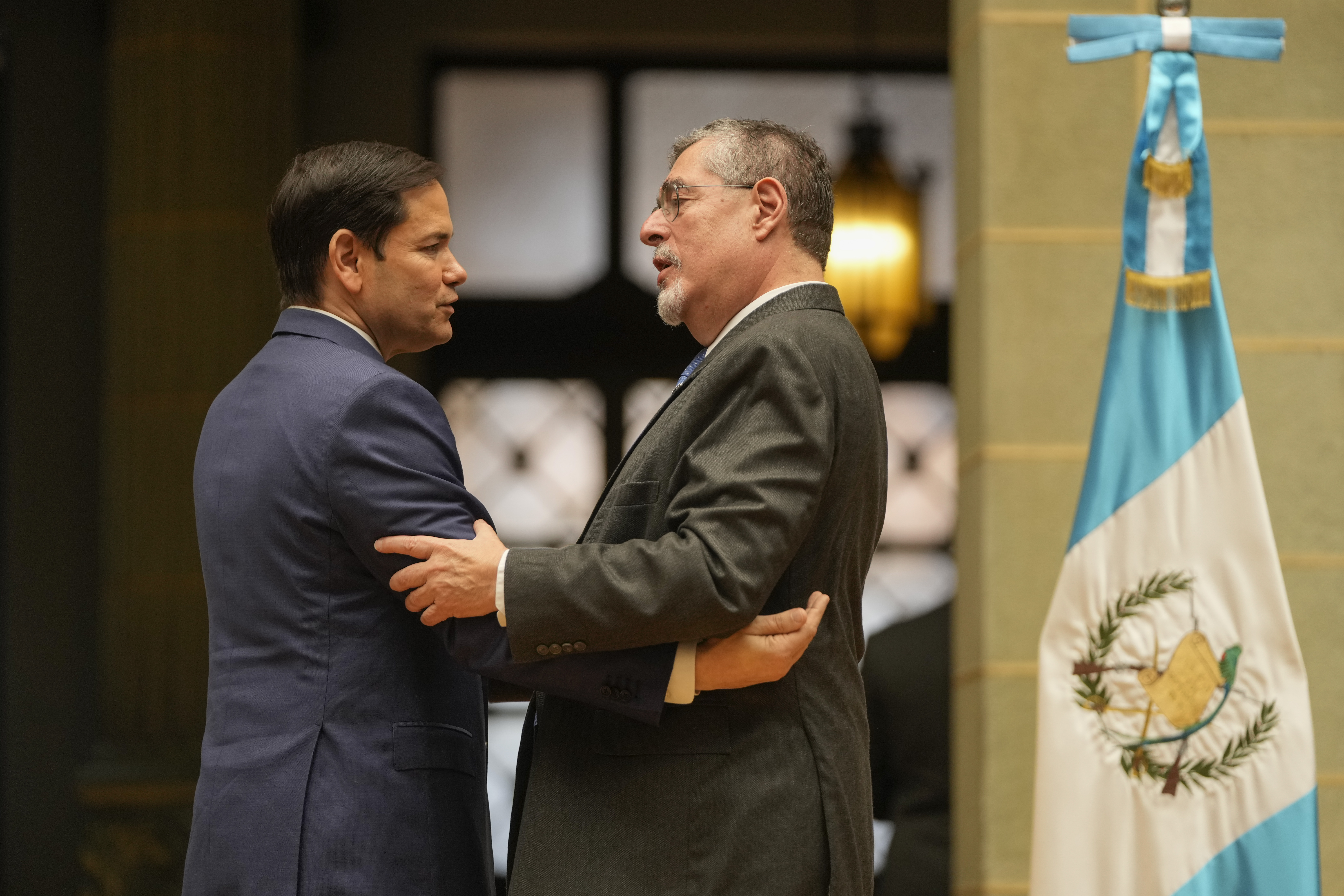 Bernardo Arevalo and Marco Rubio shake hands in front of a Guatemalan flag.
