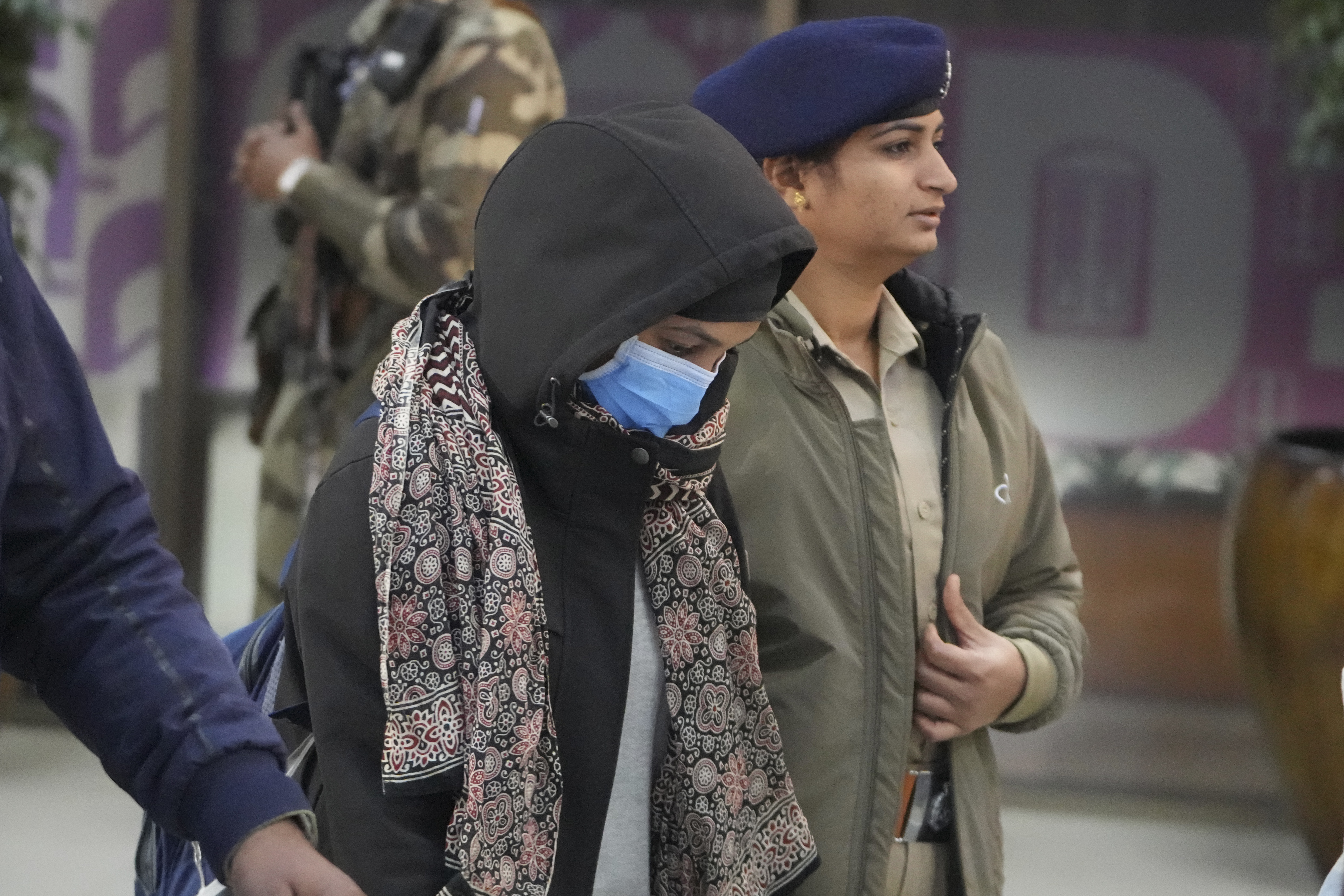 An Indian police official escorts an immigrant woman, wearing a mask.