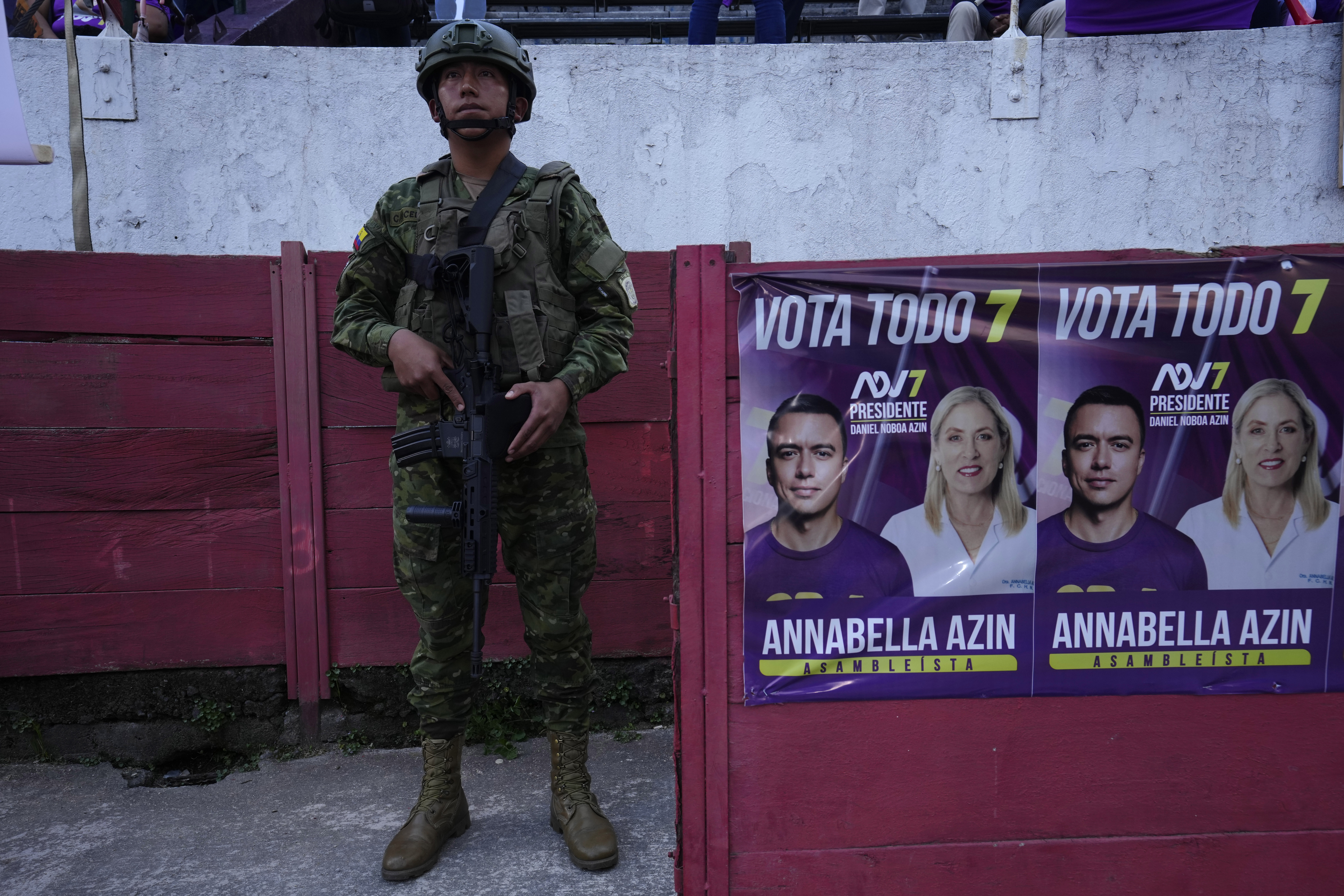A soldier stands next to posters for Daniel Noboa