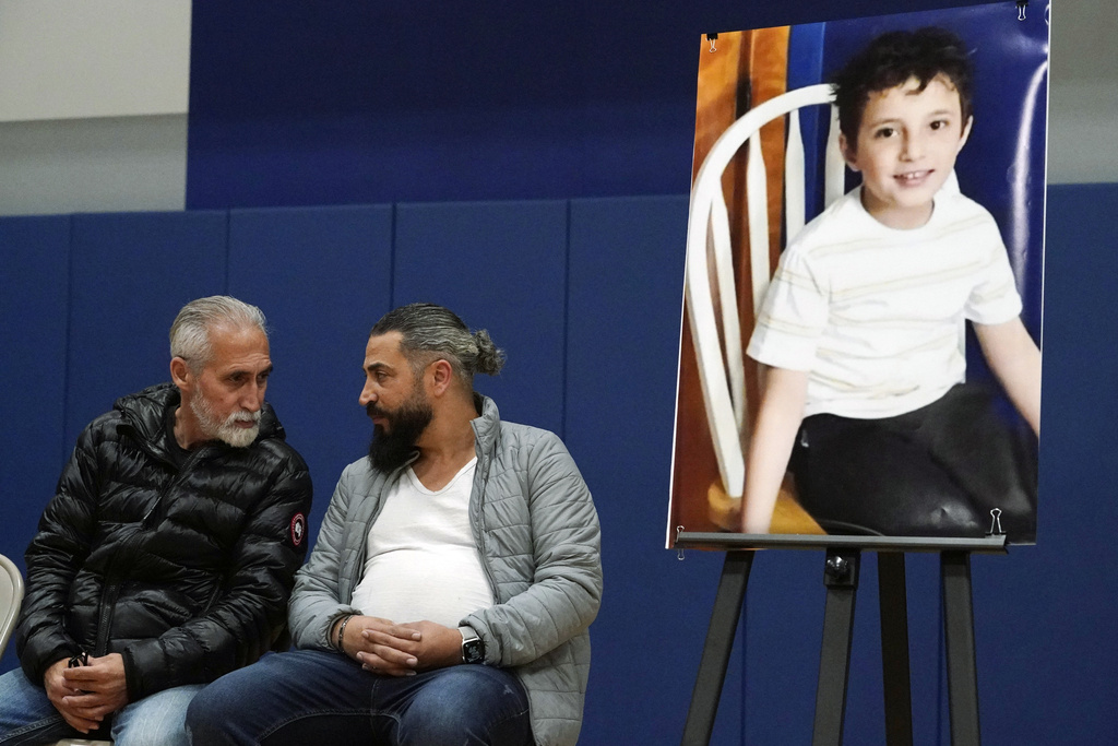 two men sit next to a portrait of a young boy sitting on a chair