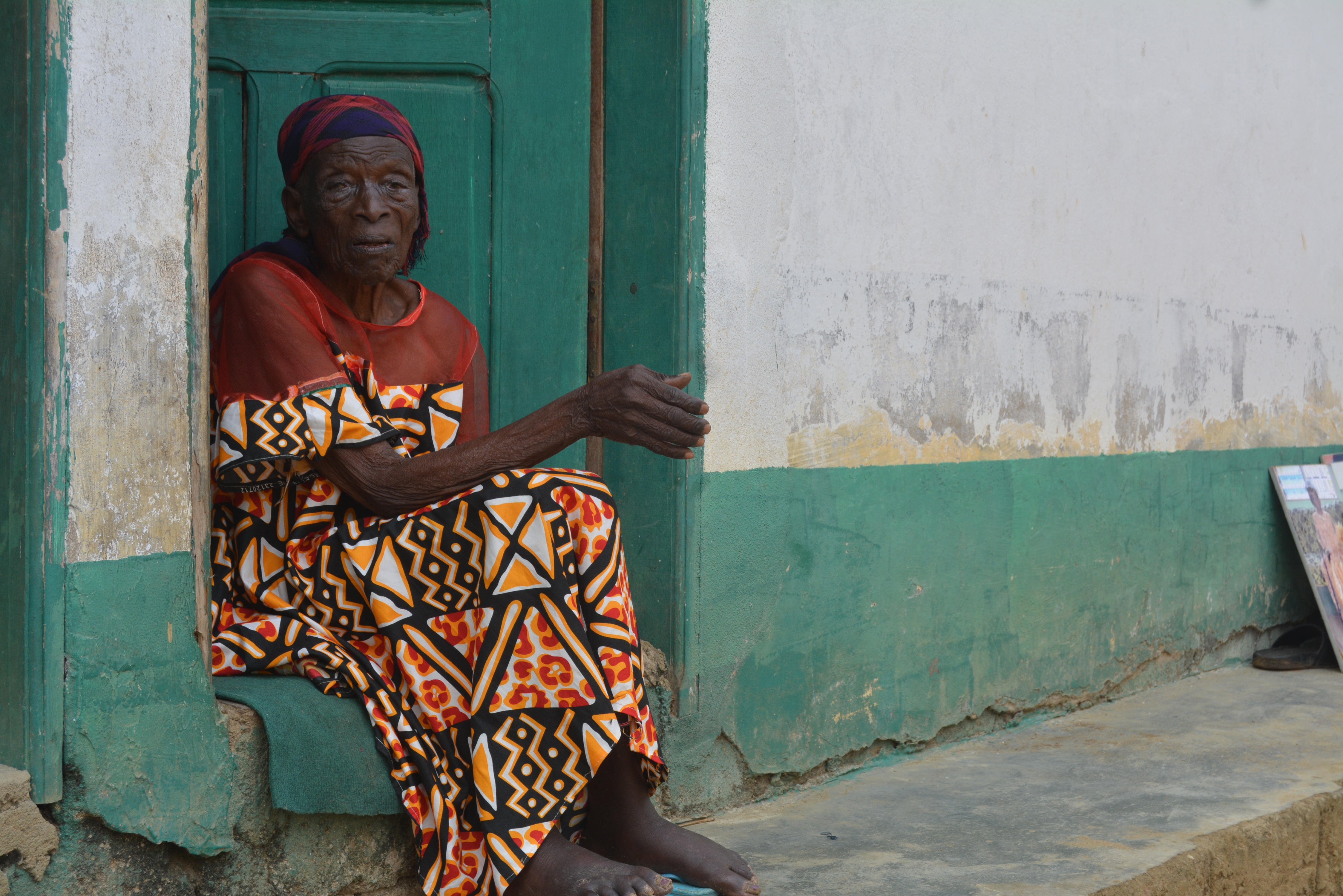 Atemafac Anathasia Tanjuh sits on a doorstep and gestures.