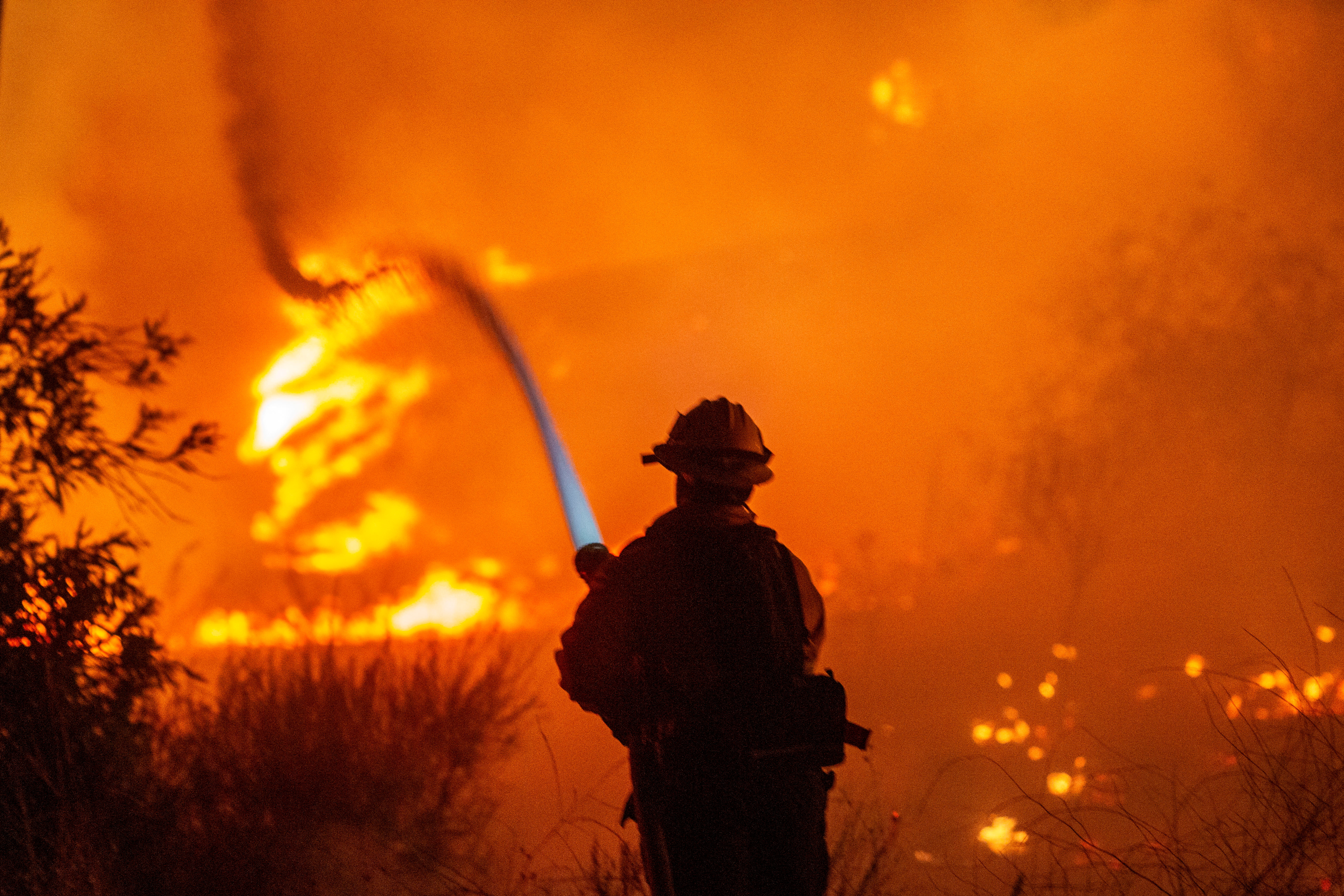 A firefighter points a hose into the flames
