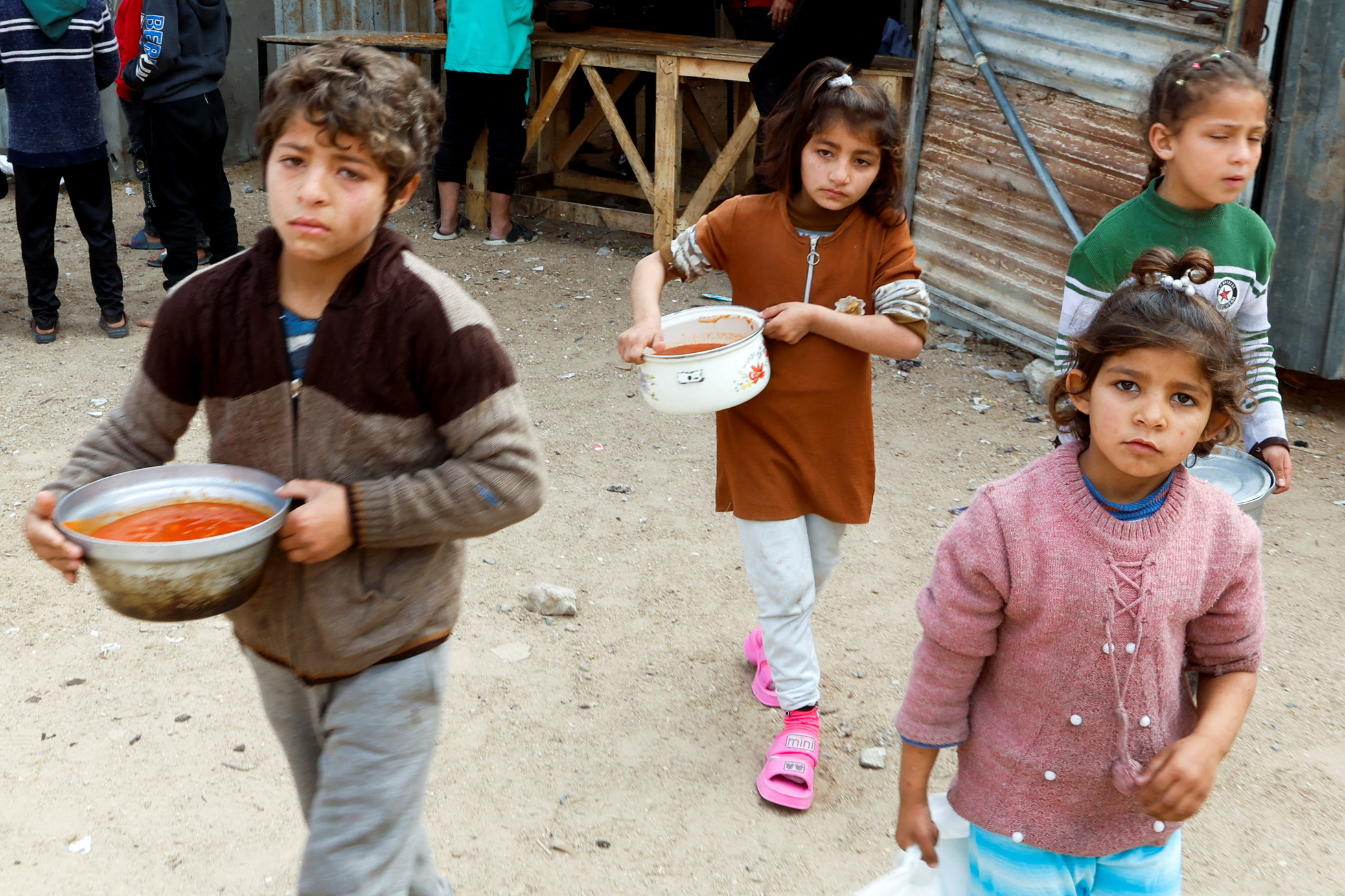 four children hold pots near makeshift shelters