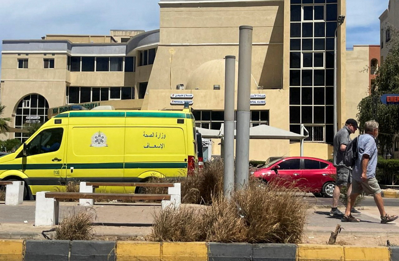 People walk next to an ambulance in front of a hospital.